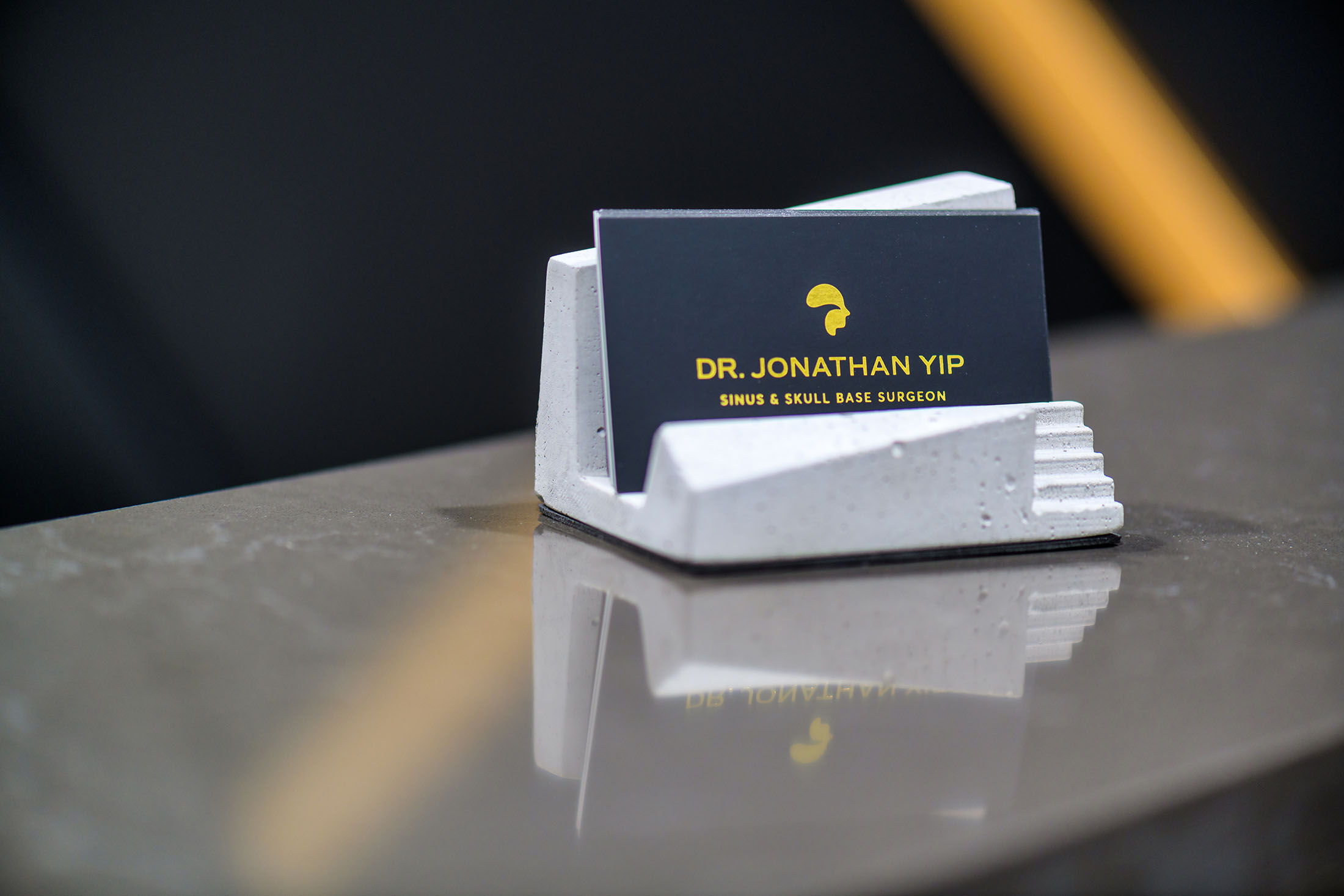 A close-up of Dr. Jonathan Yip’s branded business card displayed in a stylish concrete cardholder, highlighting his professional identity.