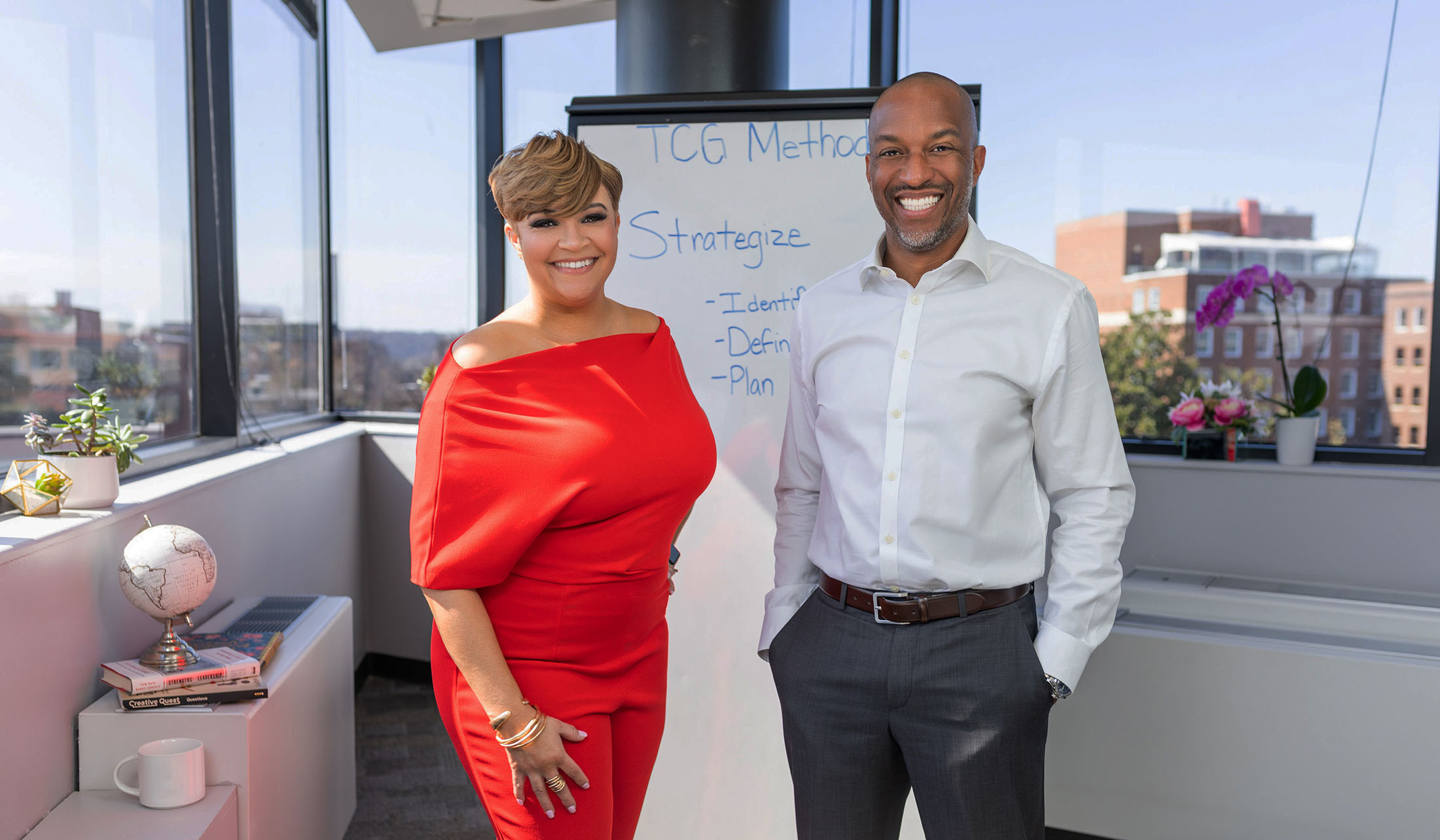 Two smiling professionals representing The CODE Group, standing in an office setting with a whiteboard displaying their strategic process.