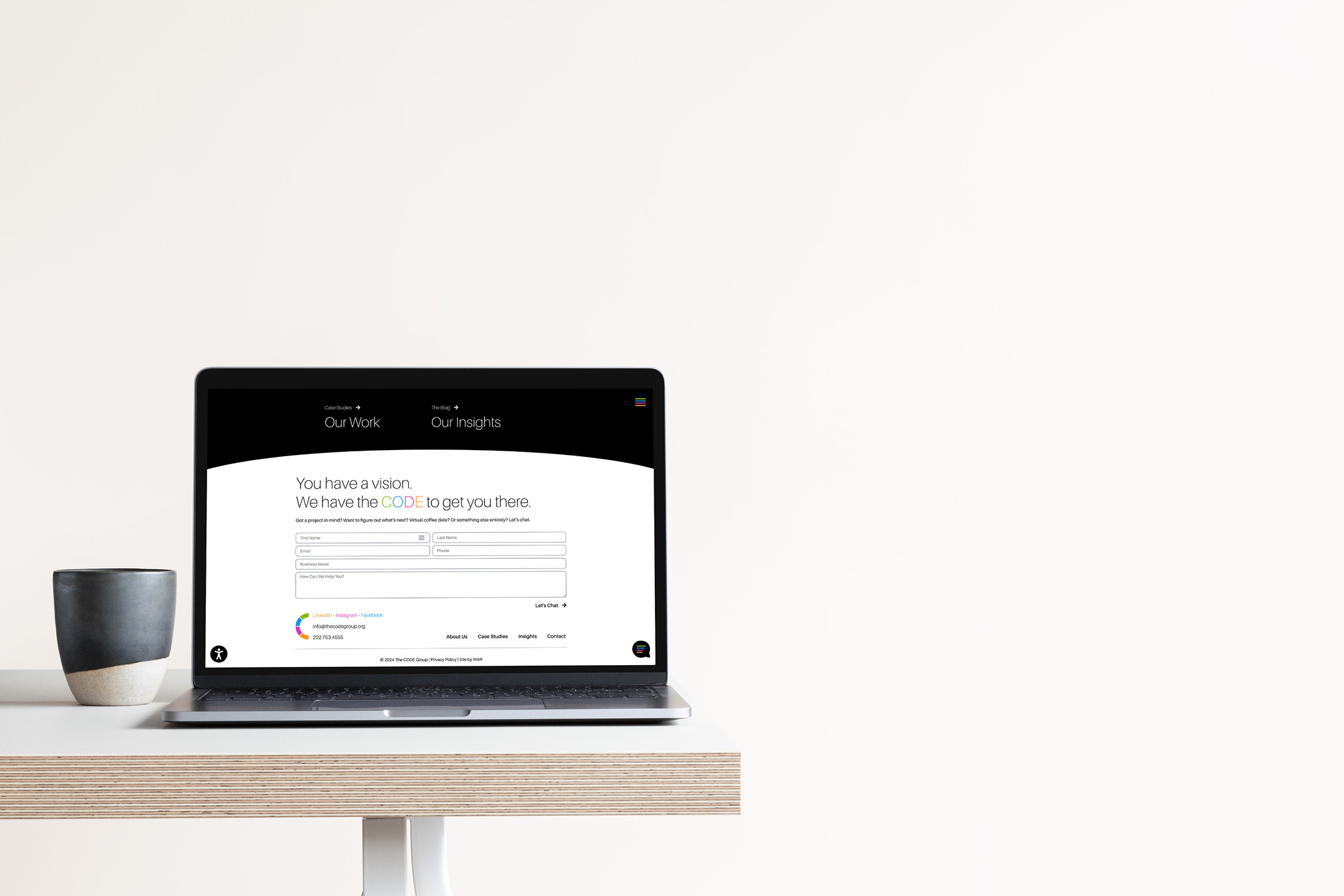A laptop on a minimalist desk setup presenting The CODE Group’s client success stories and “Our Insights” section, complemented by a black coffee mug nearby.