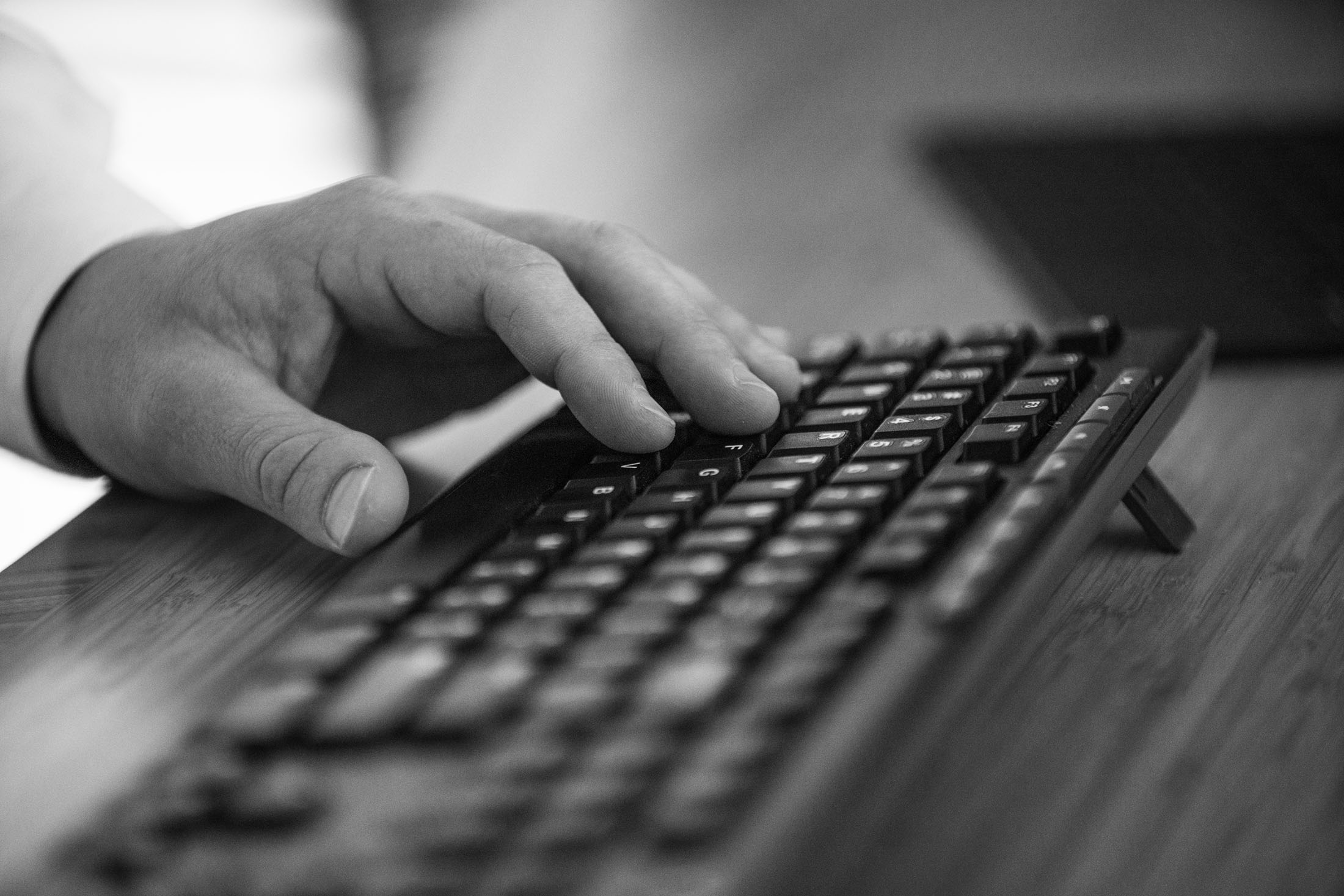 A close-up black-and-white photo of a hand typing on a keyboard, symbolizing professional services.