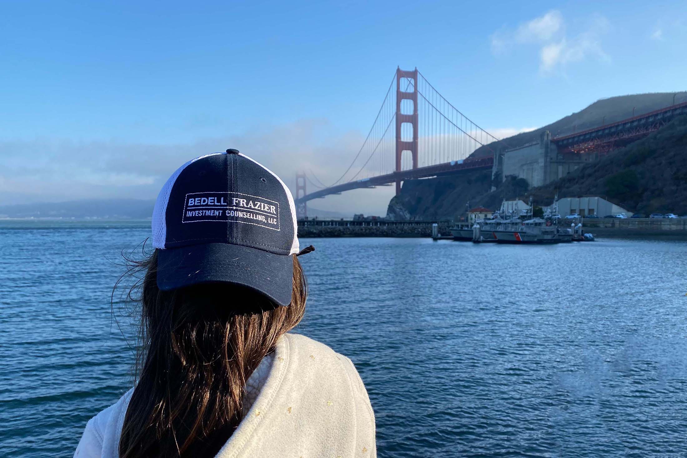 Person wearing a navy blue Bedell Frazier hat with the Golden Gate Bridge and a clear blue sky in the background.