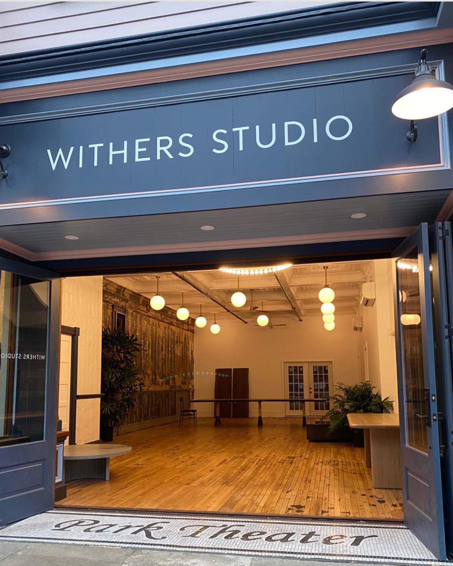 Open workshop with Withers Studio branding above, showcasing spacious design with hardwood floors and industrial lighting.