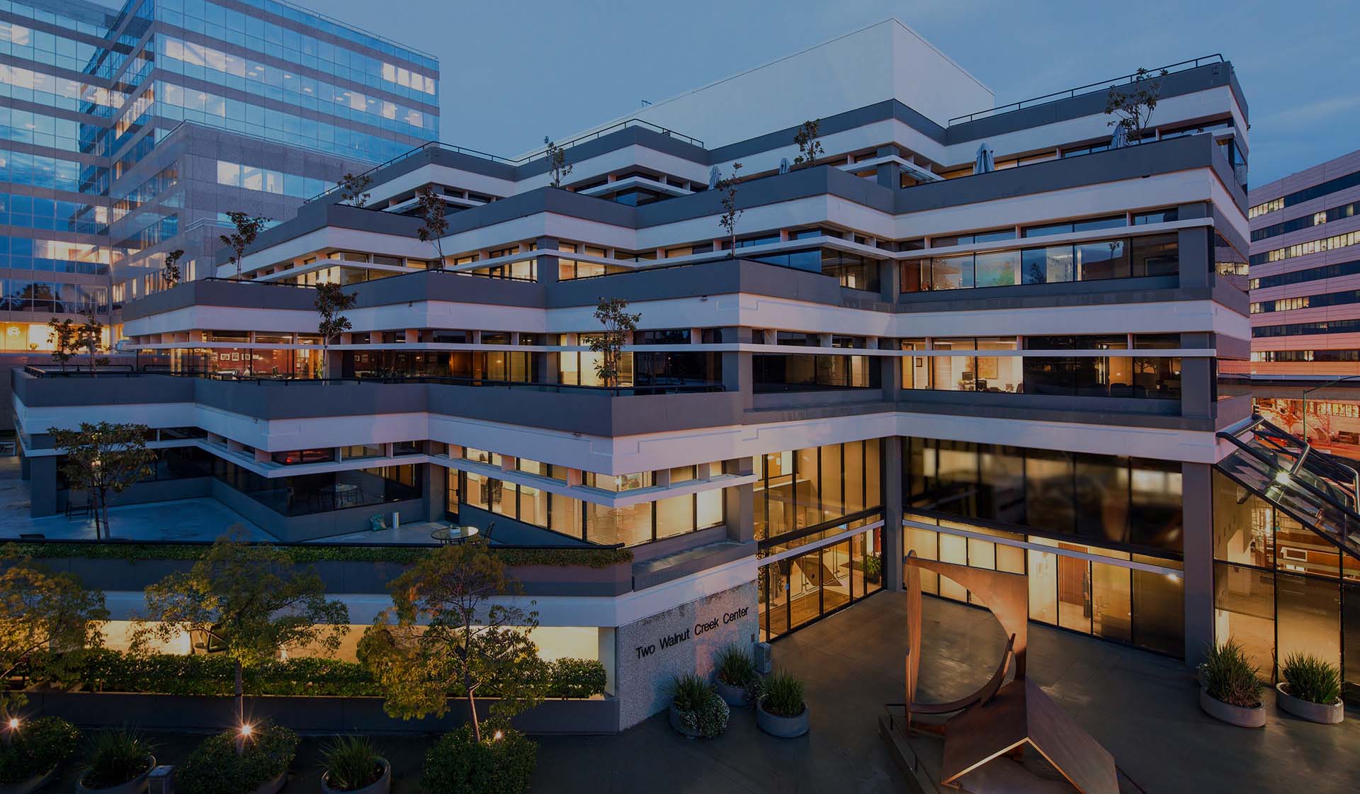 Exterior view of the Bedell Frazier Investment Counselling office building located in Walnut Creek, California, showcasing a modern architectural design with illuminated windows and landscaped terraces during twilight.