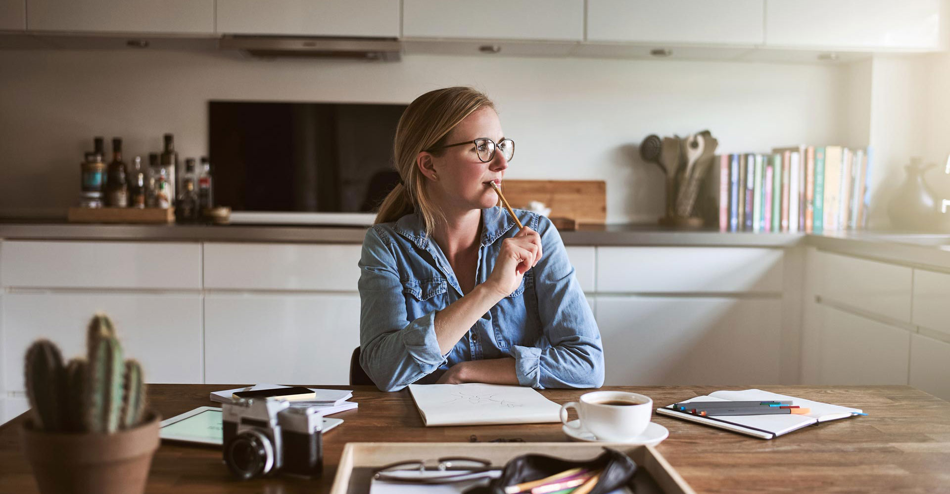 Thoughtful creative professional sitting in a kitchen workspace, sketching ideas for branding and brand identity design with tools and coffee on the table.