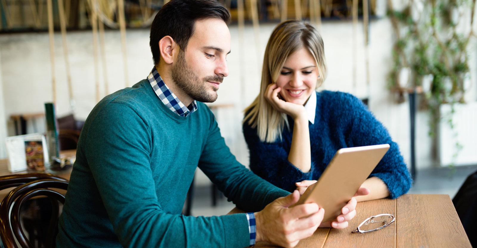 Man and woman collaborating in a casual setting, reviewing a tablet to plan guest blog posts and strengthen branding through strategic content partnerships.