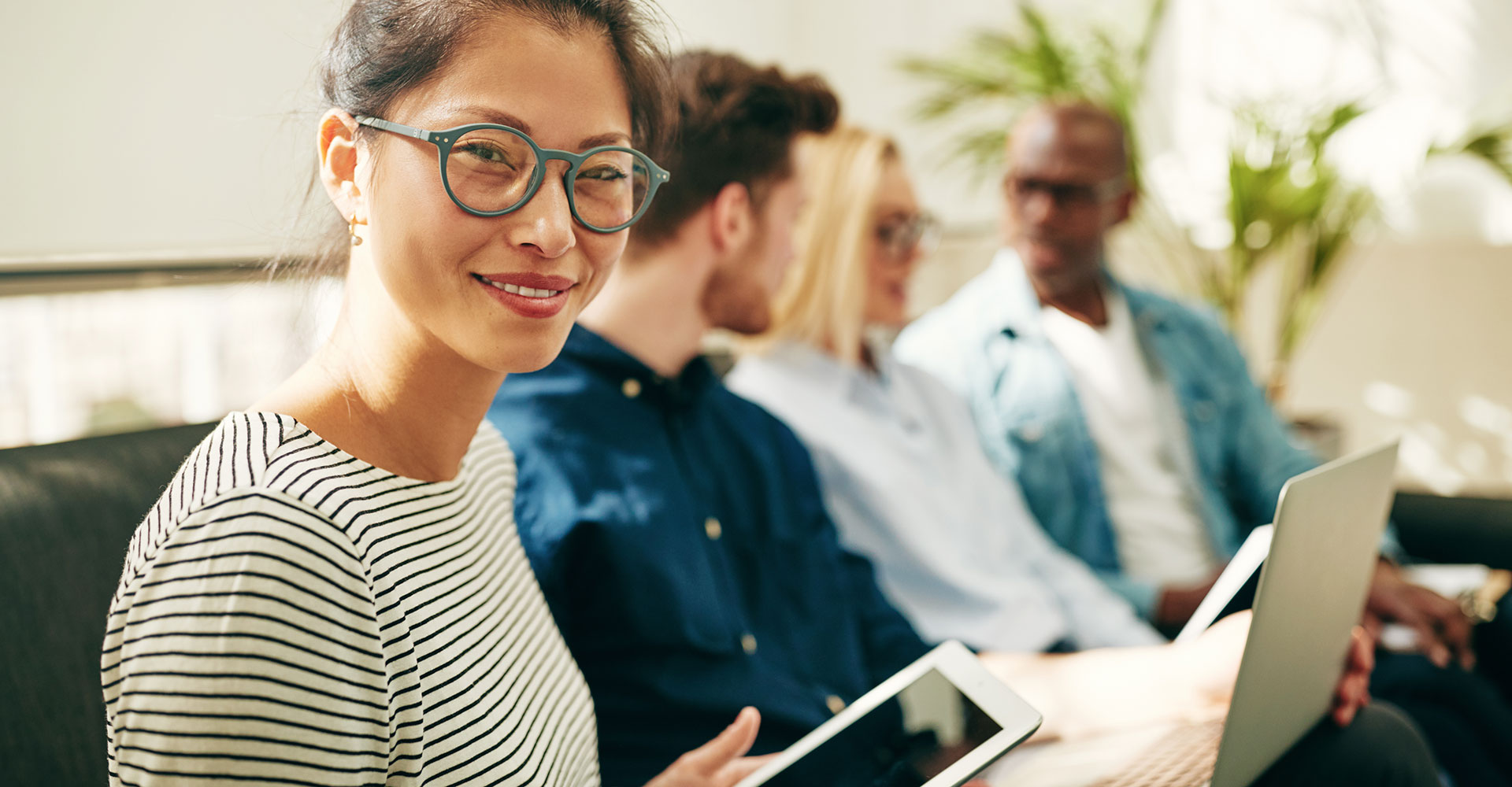 Smiling woman holding a tablet during a collaborative meeting, showcasing professional engagement and online social networking strategies for branding and website design.