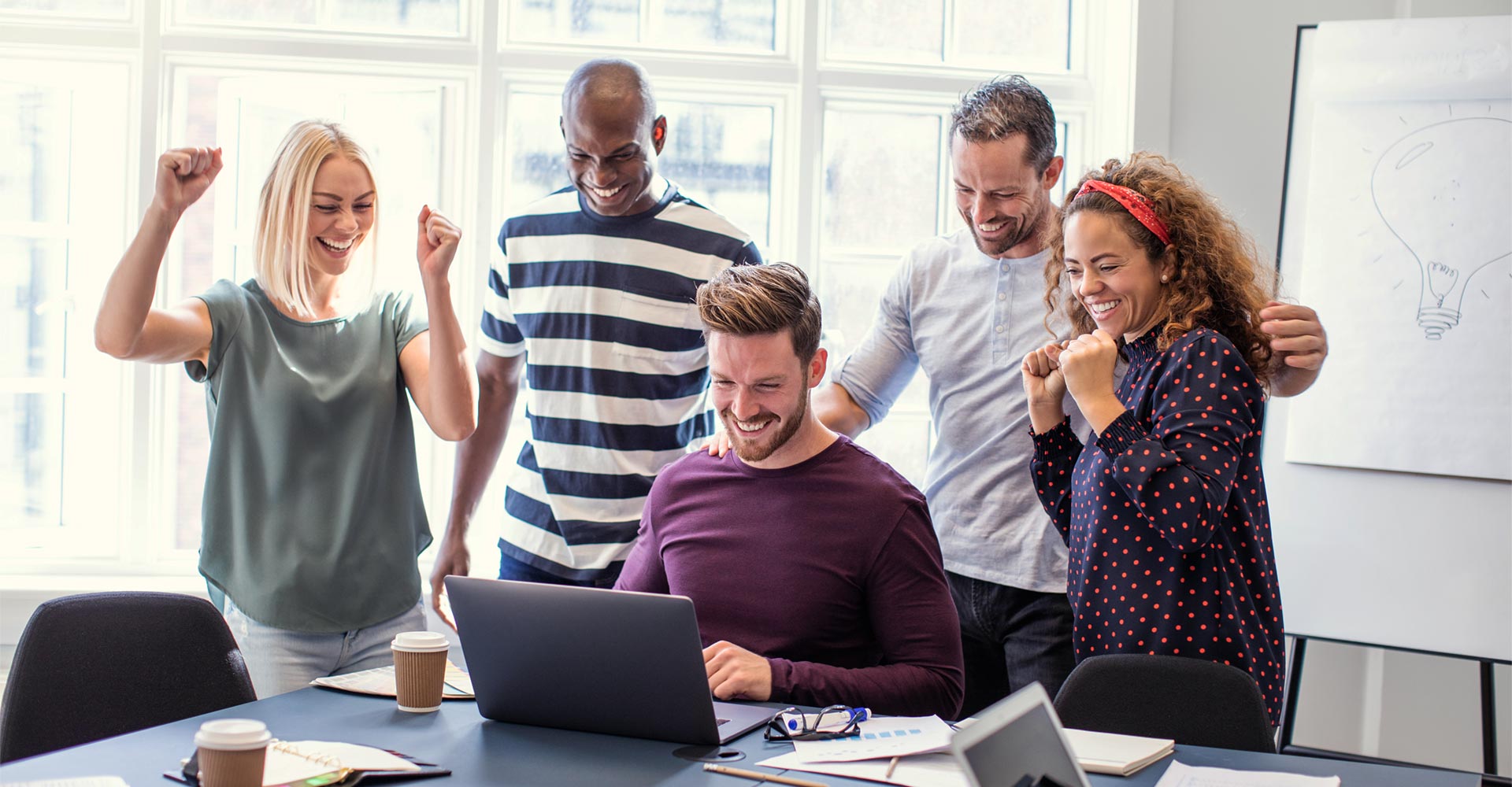 Team celebrating a successful project around a laptop, showcasing collaboration and creative community building for branding and social media strategies.