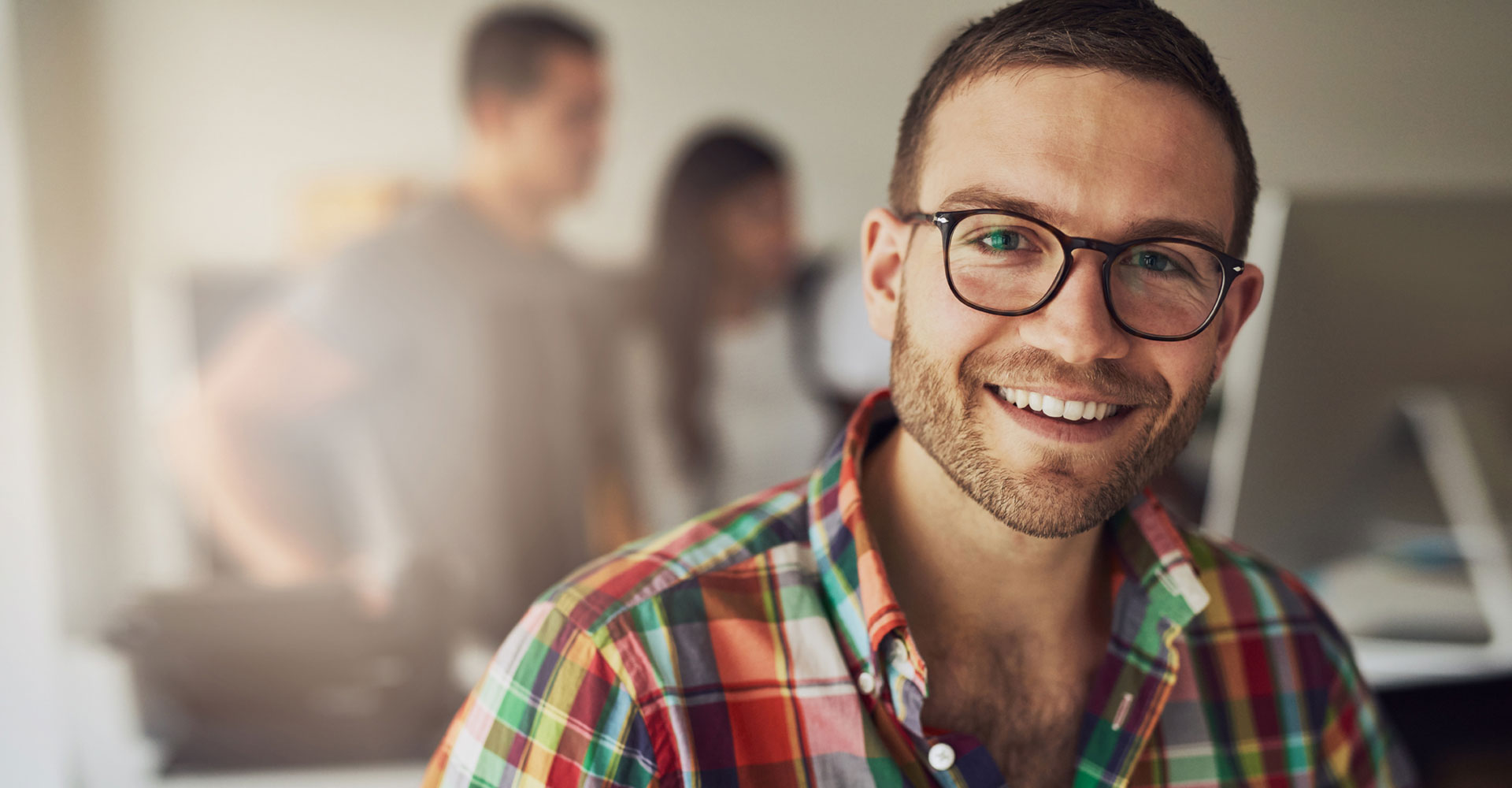 Smiling professional in a vibrant plaid shirt at a modern workspace, representing personal branding and the impact of investing in creative brand design strategies.