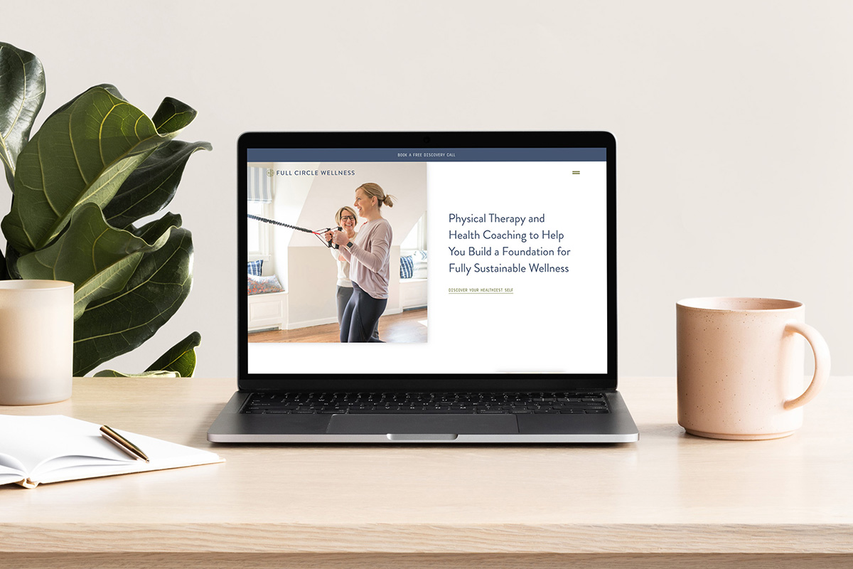 Laptop displaying the Full Circle Wellness website featuring physical therapy and health coaching services, with a woman assisting a client with an exercise. The scene includes a cozy interior with a plant and a cup on a desk.