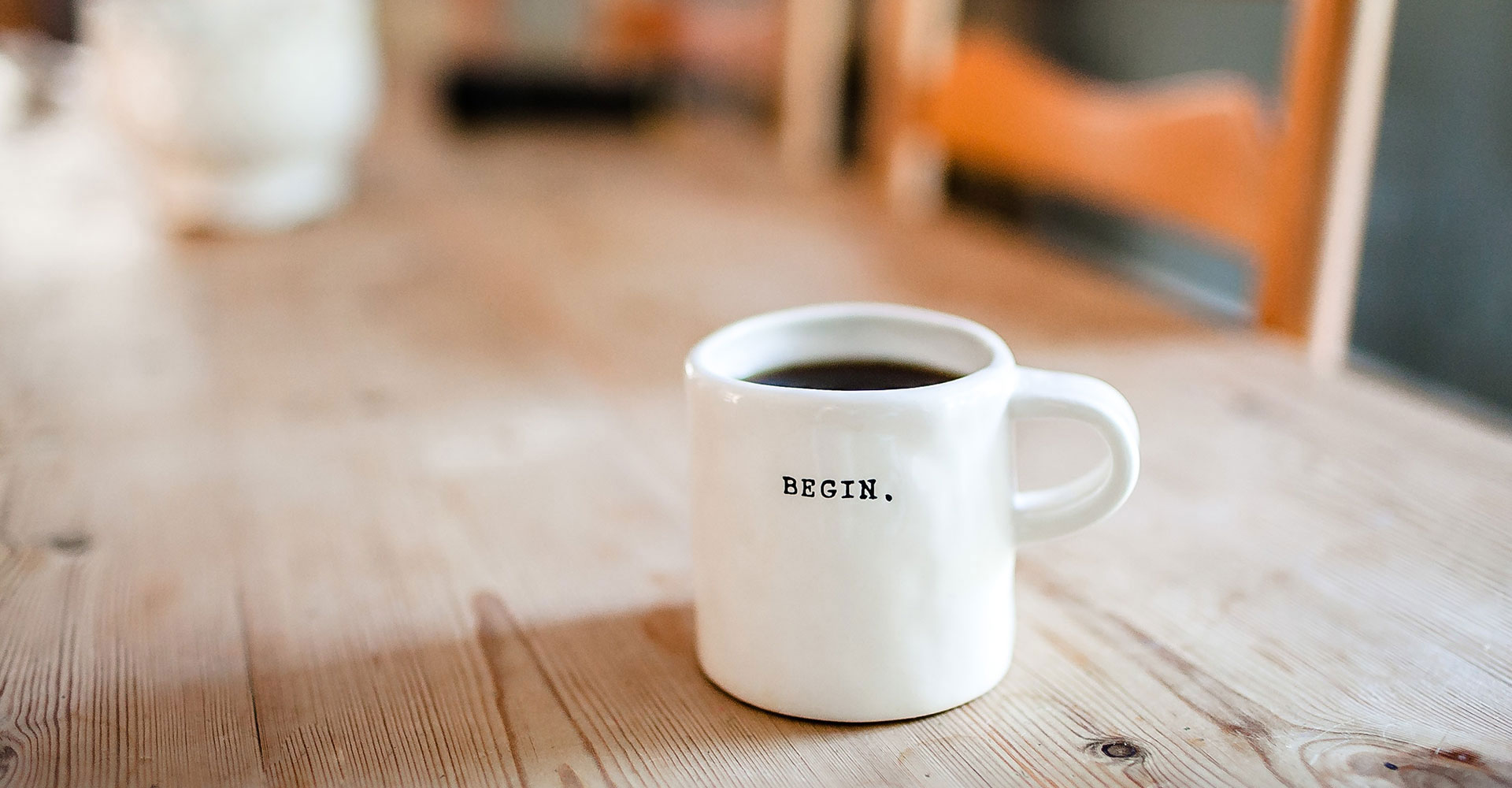 White coffee mug with the word ‘Begin’ printed on it, placed on a wooden table, symbolizing the start of branding and website design projects with a clear purpose.