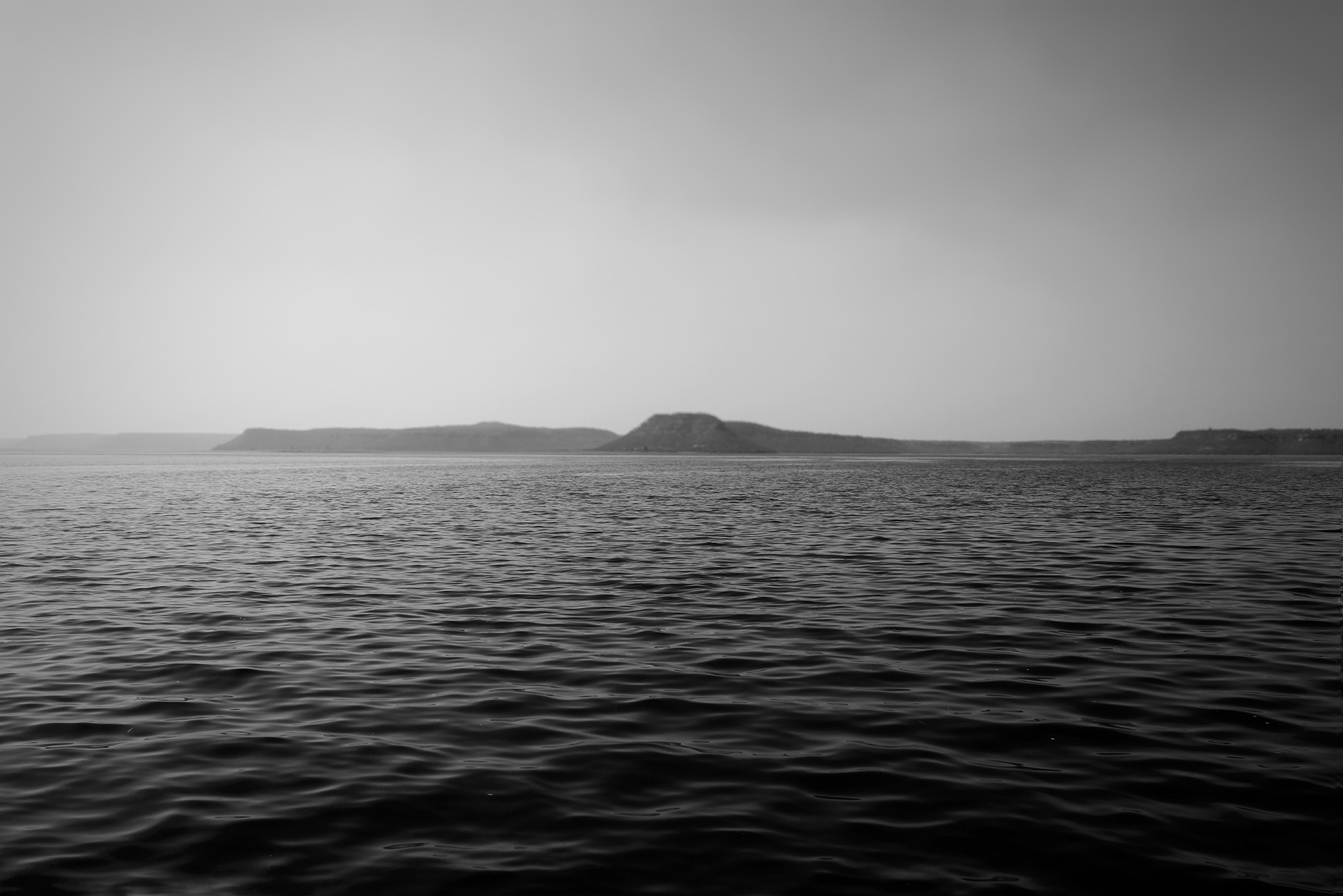 Black-and-white image of a vast ocean with an island in the distance, creating a sense of tranquility and perspective.