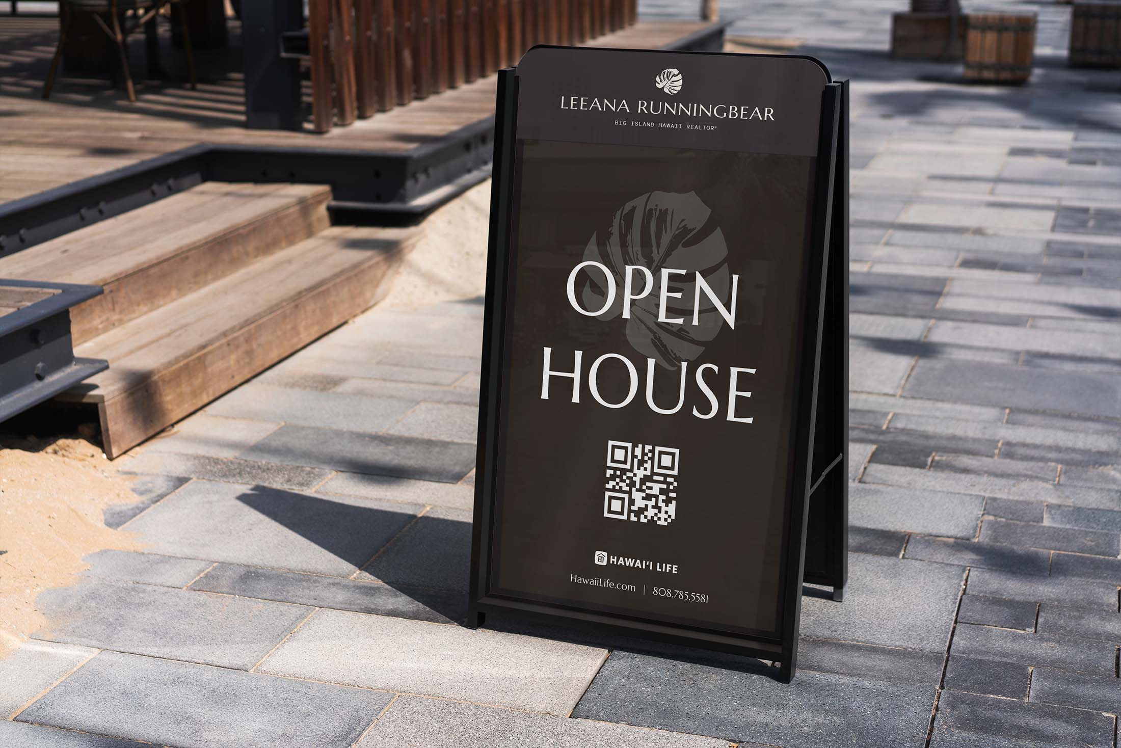 Dark brown open house signboard for Leeana Runningbear Realtor®, positioned on a modern stone pavement and featuring a QR code for more property details.