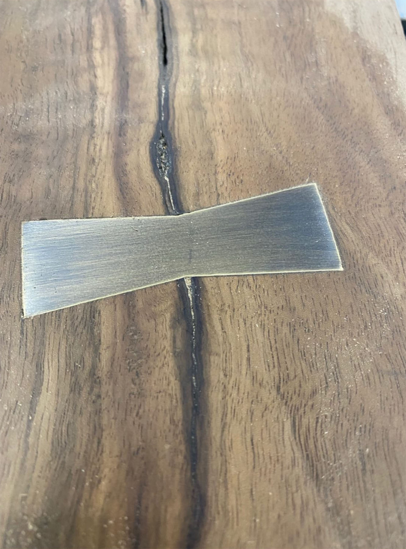 Close-up of a brass bowtie inlay on a handcrafted wood table by Withers Studio, highlighting refined craftsmanship and custom furniture design.