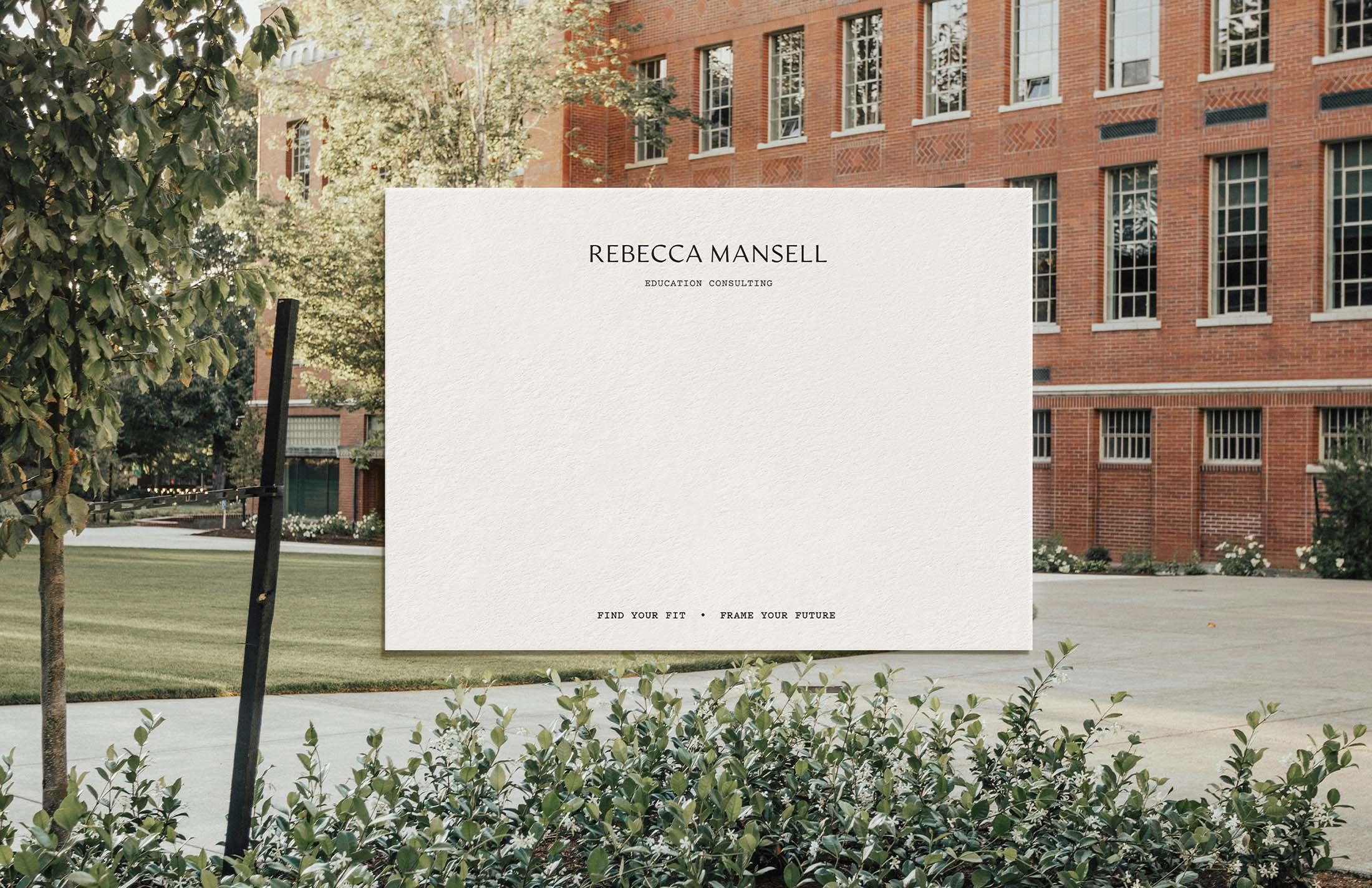 A poster design placed outdoors, highlighting the Rebecca Mansell Consulting branding and tagline, “Find Your Fit, Frame Your Future,” against a backdrop of greenery and a red-brick building.