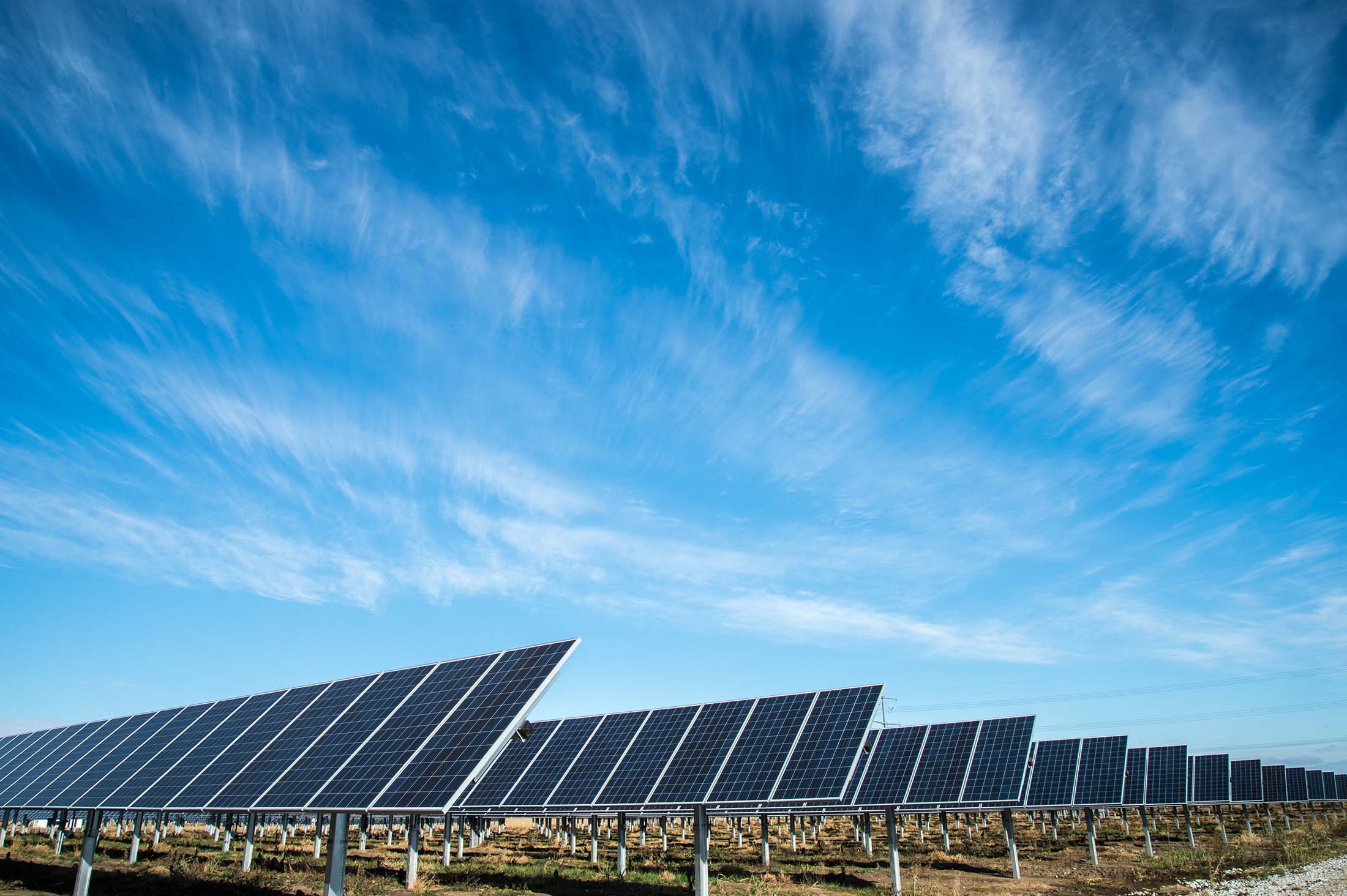 Wide-angle view of solar panels under a vibrant blue sky with scattered clouds, highlighting a clean energy source.