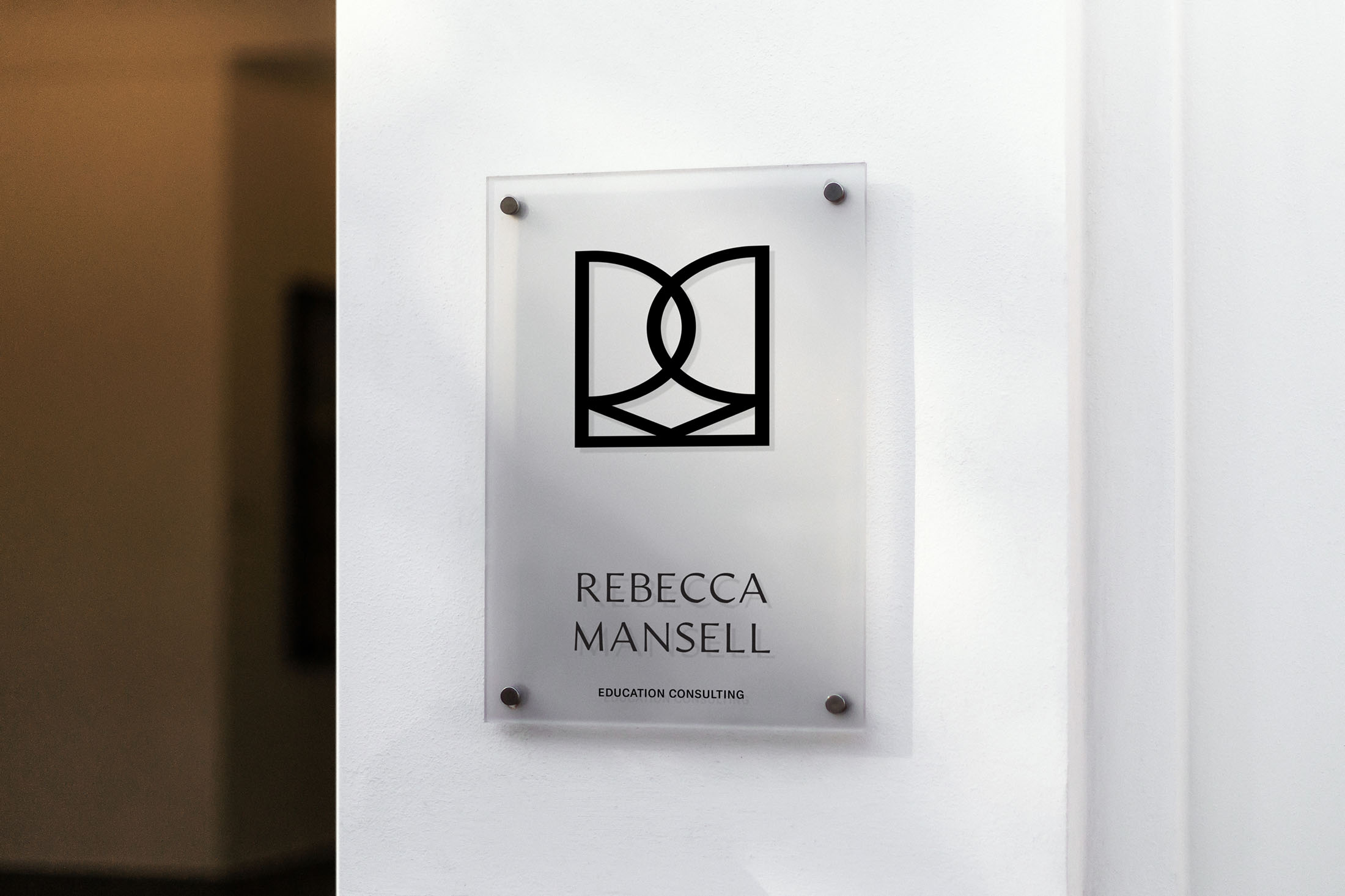 A sleek, frosted acrylic office sign displaying the Rebecca Mansell Consulting logo and name, mounted on a white wall with silver brackets.