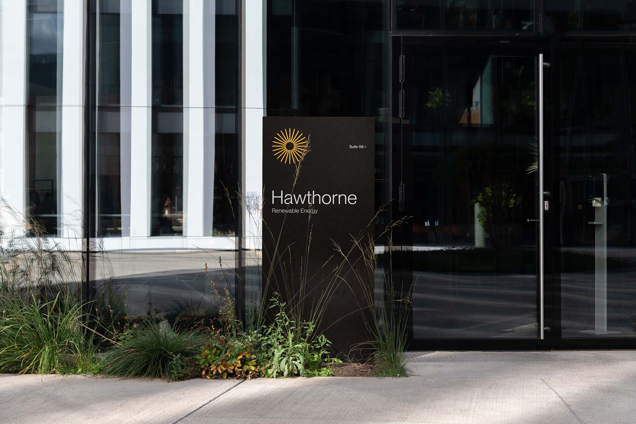 Hawthorne Renewable Energy logo and name displayed on sleek black signage outside a modern glass building surrounded by plants.