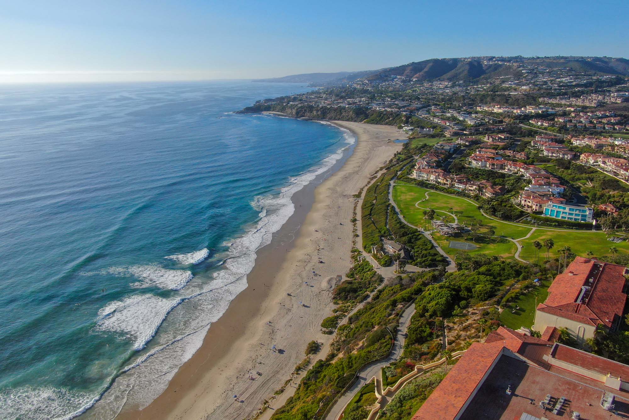 Aerial view of a coastal landscape featuring a long sandy beach, lush greenery, and upscale homes, representing Salt Creek Partners’ regional inspiration.