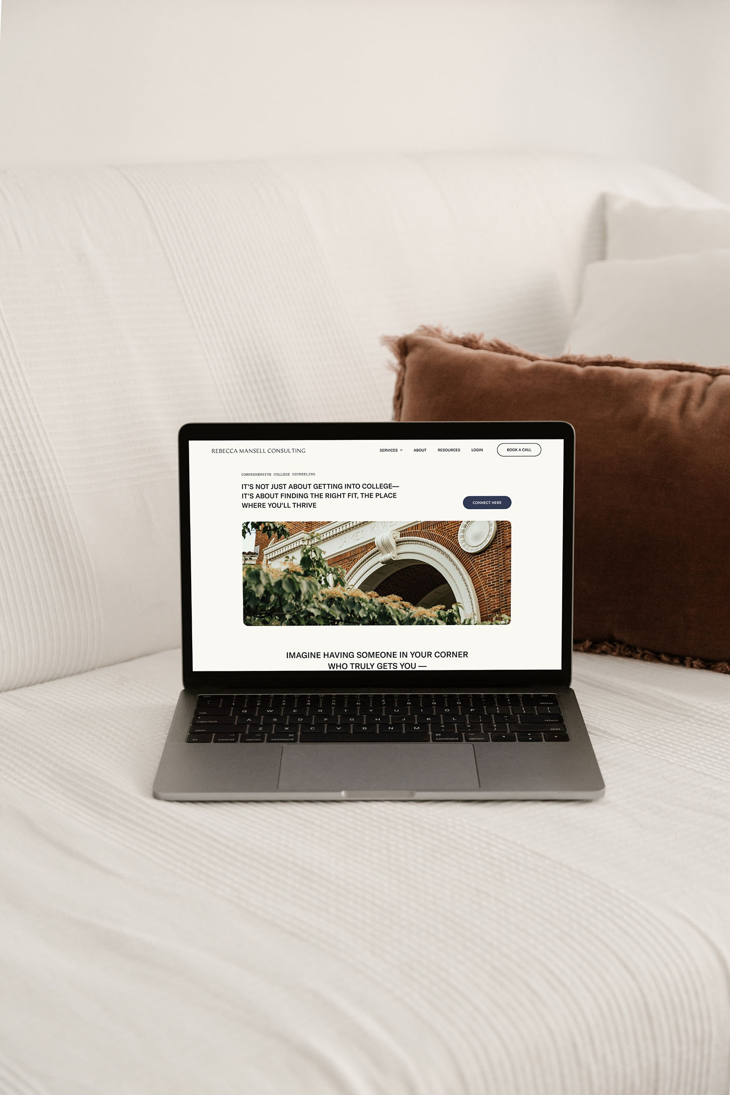 A laptop on a white couch displaying the Rebecca Mansell Consulting website with the tagline “It’s not just about getting into college—it’s about finding the right fit.” A brown pillow sits in the background.