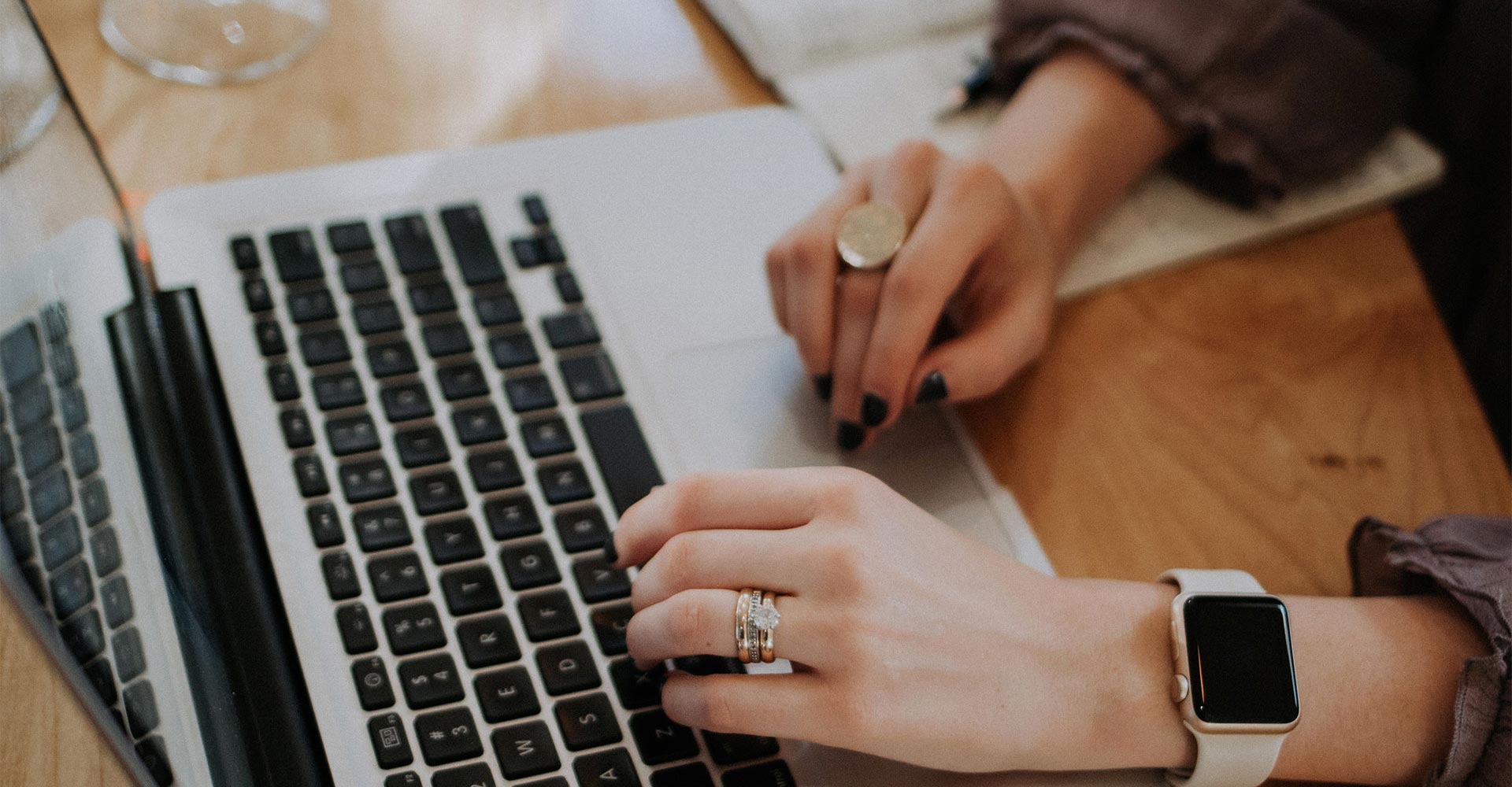 Close-up of hands typing on a laptop, wearing rings and a smartwatch, symbolizing attention to detail and strategy in crafting effective home page content for branding