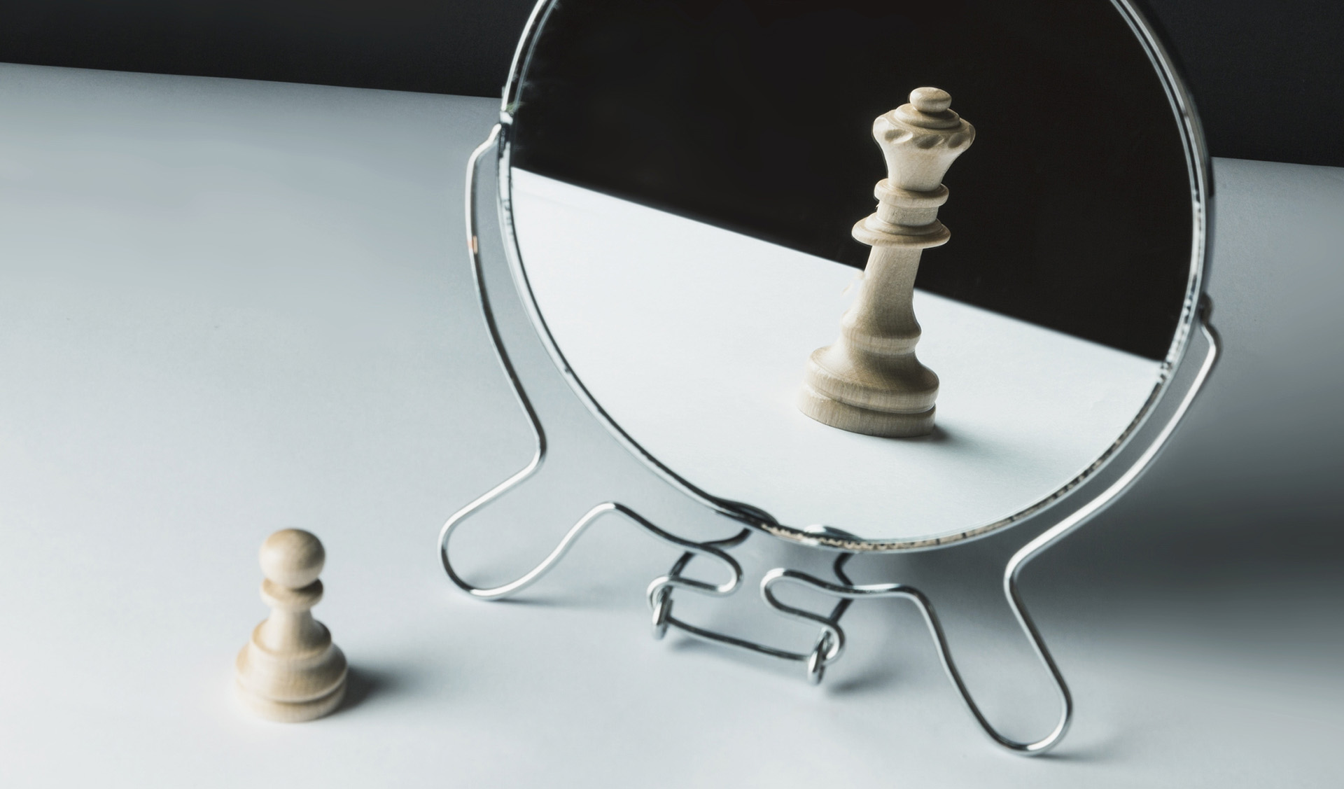 A wooden pawn chess piece reflecting as a king in a tabletop mirror, symbolizing self-confidence and transformation.