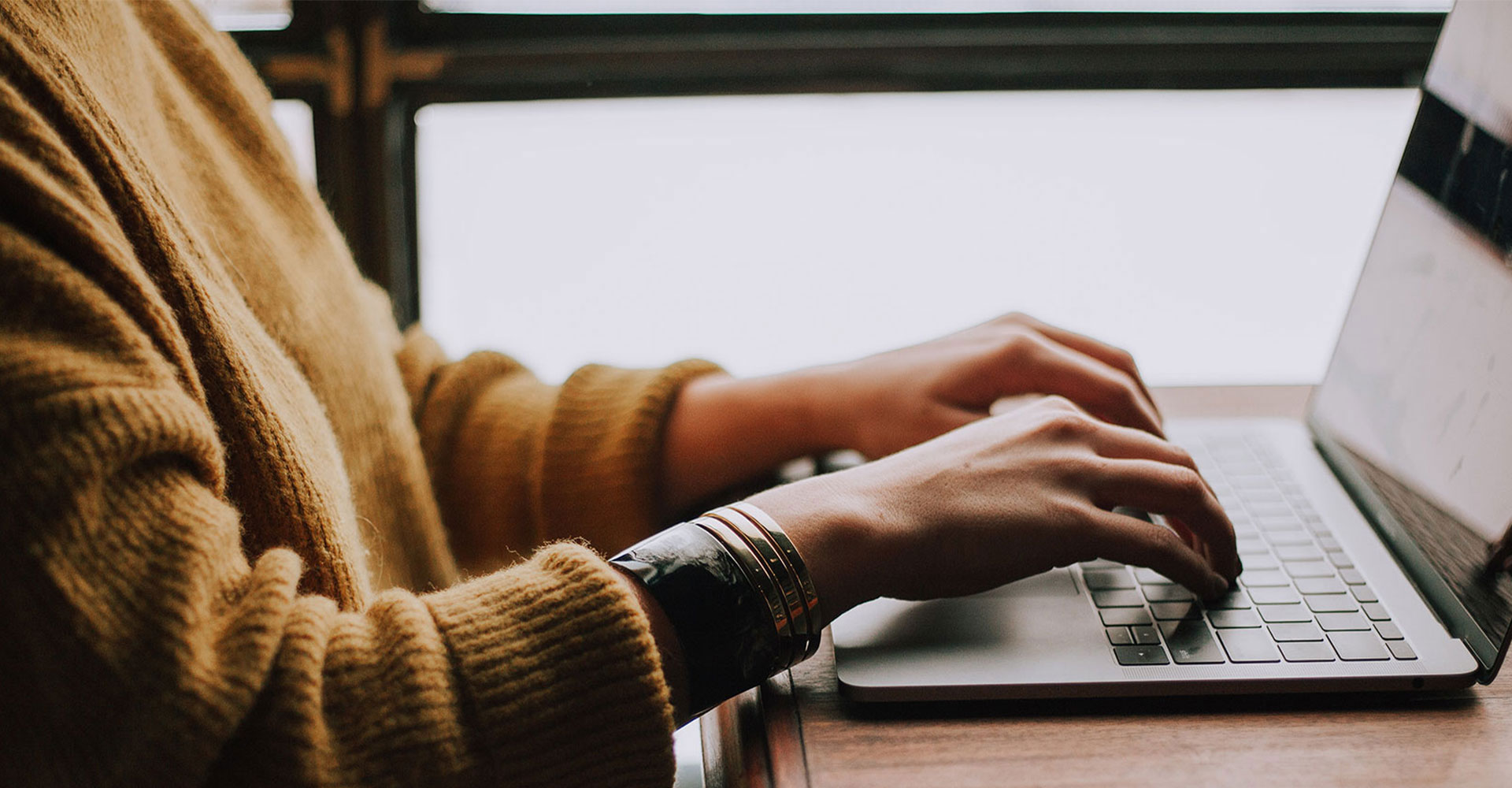 Close-up of hands typing on a laptop in a cozy setting, symbolizing the thoughtful process of writing an engaging About Page for branding and storytelling.