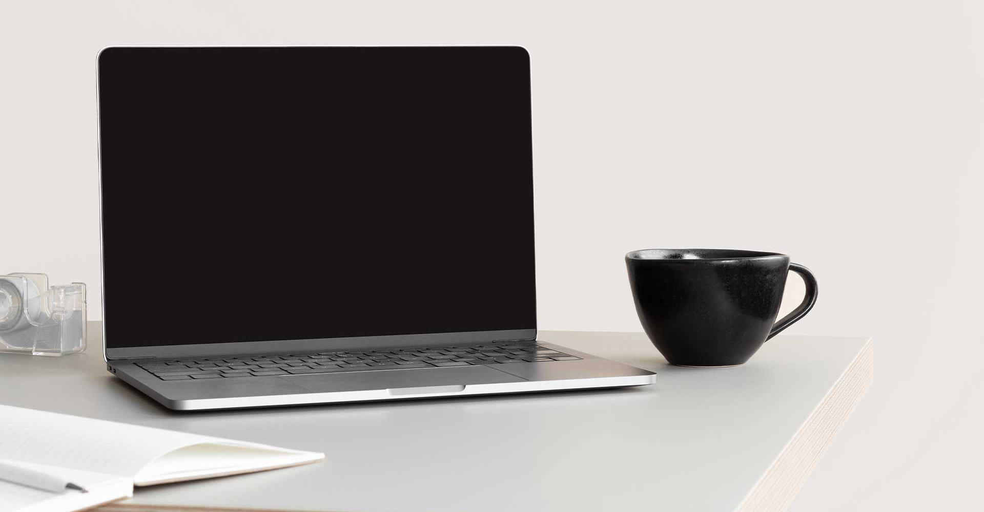 Minimalist workspace setup with a blank laptop screen, black coffee cup, and open notebook, representing online resources for small business owners.