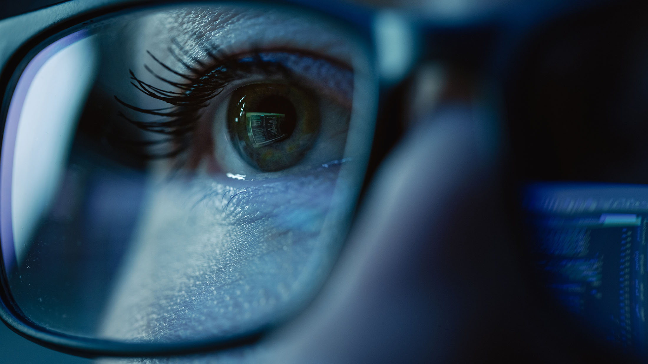 Close-up of an eye reflecting computer code on glasses, symbolizing focus and expertise in cybersecurity.