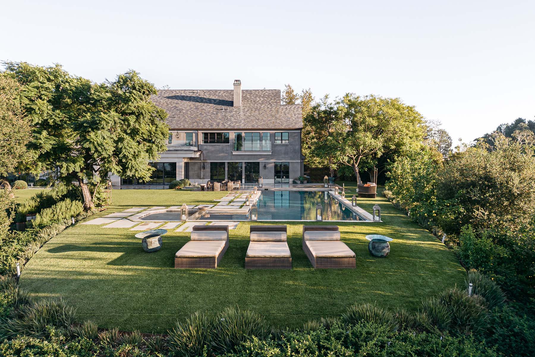 Landscape view of a modern luxury home featuring a pool, lush greenery, and outdoor lounge chairs, showcasing expert landscape architecture and eco-luxury design.