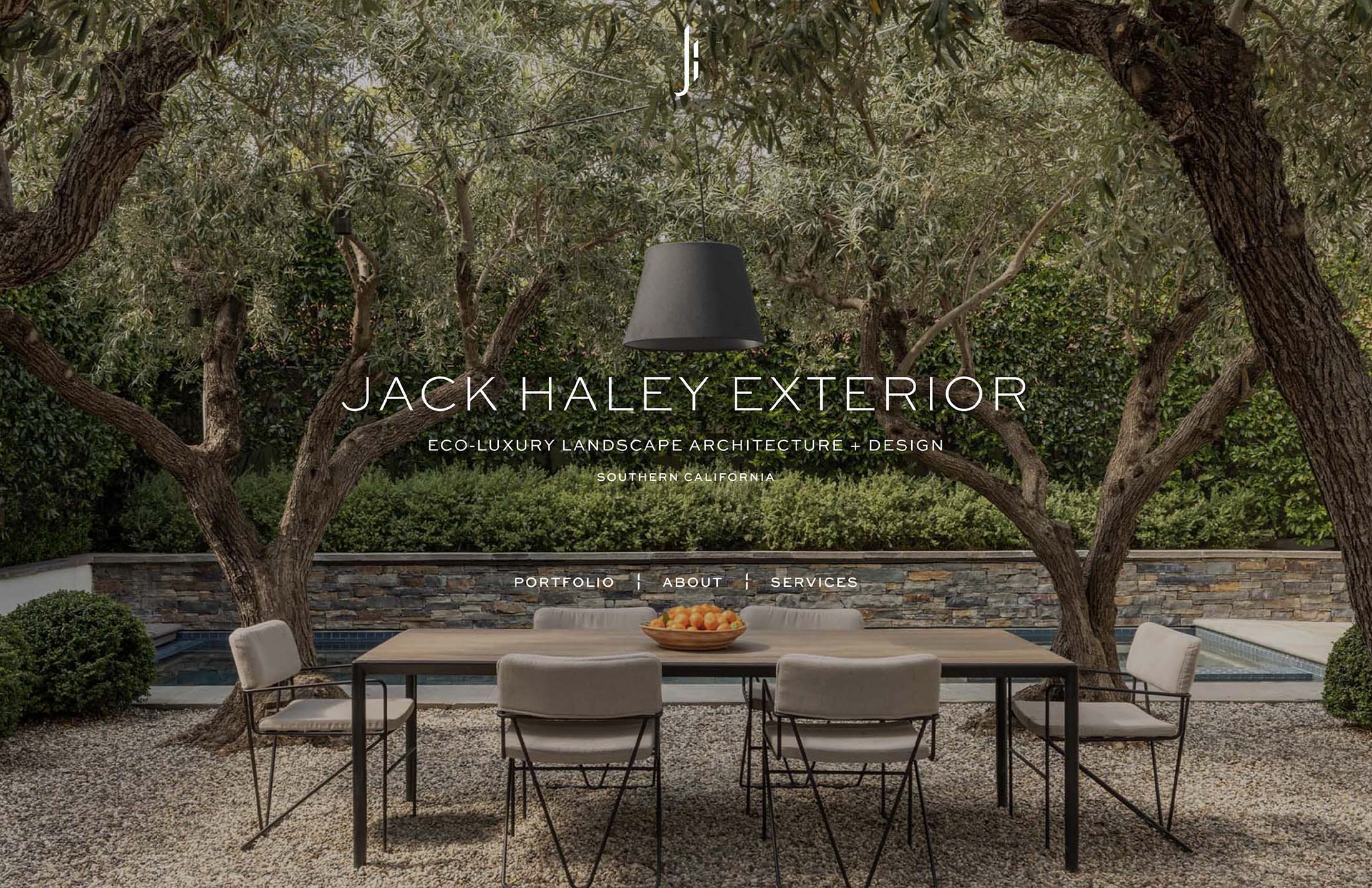 The homepage of the Jack Haley Exterior website, showcasing a serene outdoor dining area with a modern table and chairs under mature olive trees, reflecting eco-luxury landscape design.