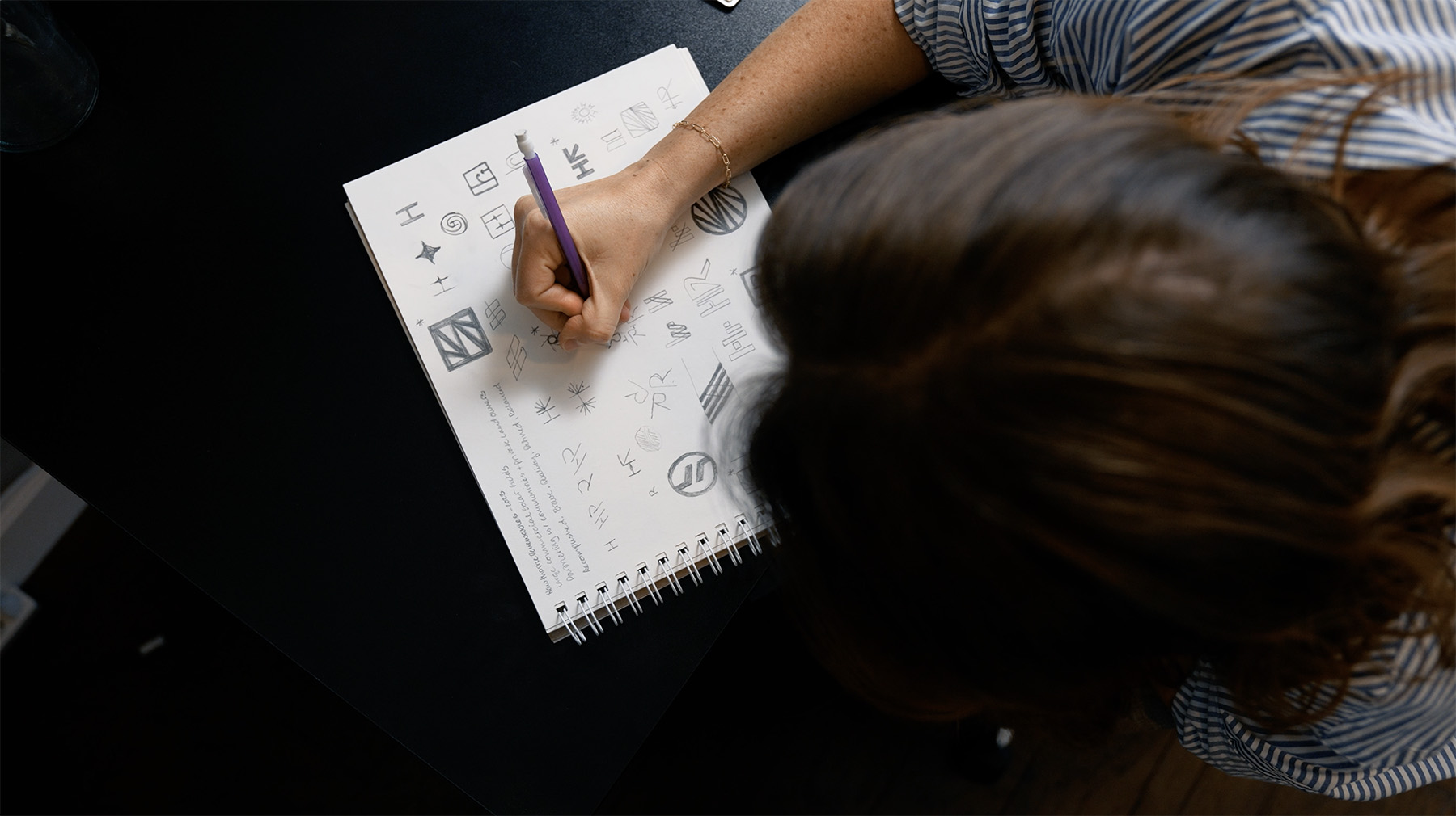 Julie Harris of Whiskey & Red sketching logo concepts in a notebook, showcasing the creative process of branding and logo design. The desk provides a minimal, focused workspace for innovative ideation.