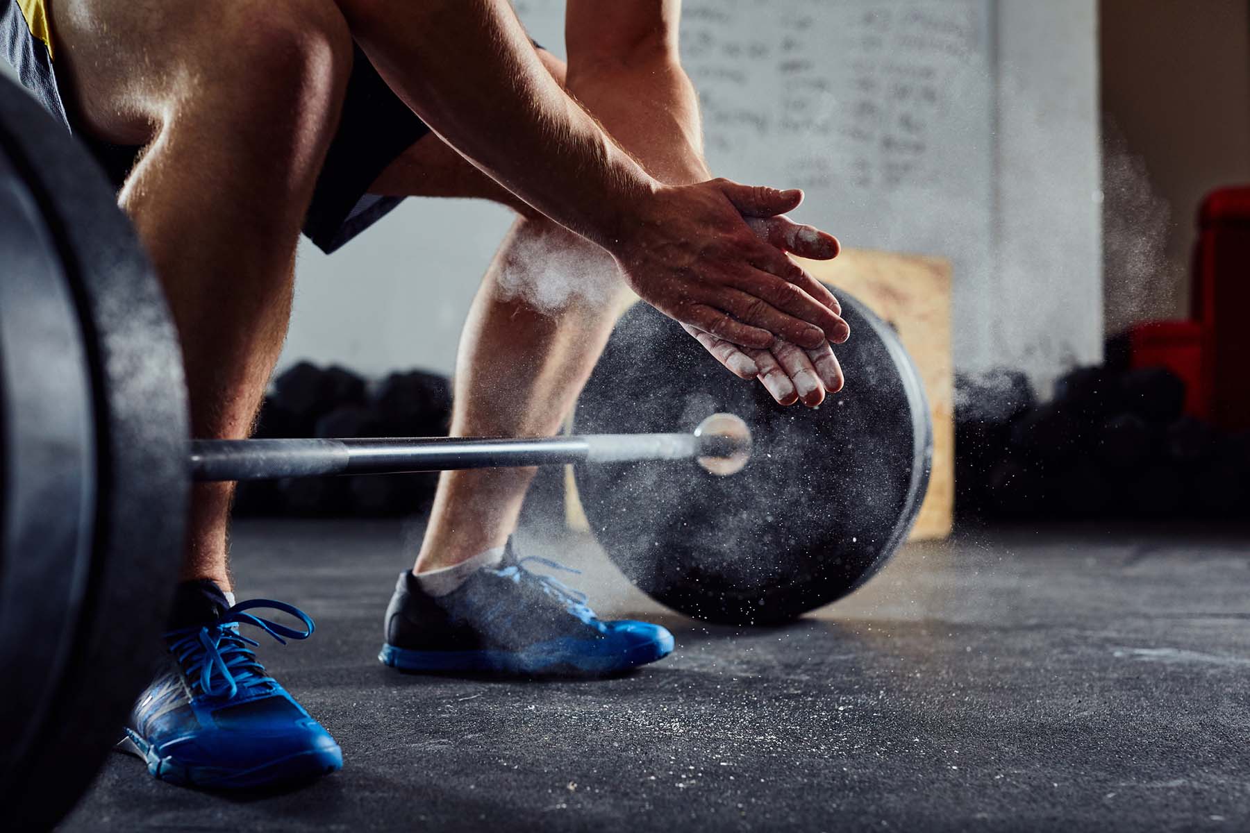 Close-up of a person preparing to lift a barbell, clapping chalked hands in a gym, symbolizing self-agency and owning one’s business and time.