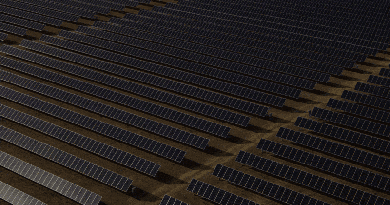 Animated brand mark over an aerial view of an expansive solar farm with rows of solar panels arranged neatly on a brown, sunlit landscape.