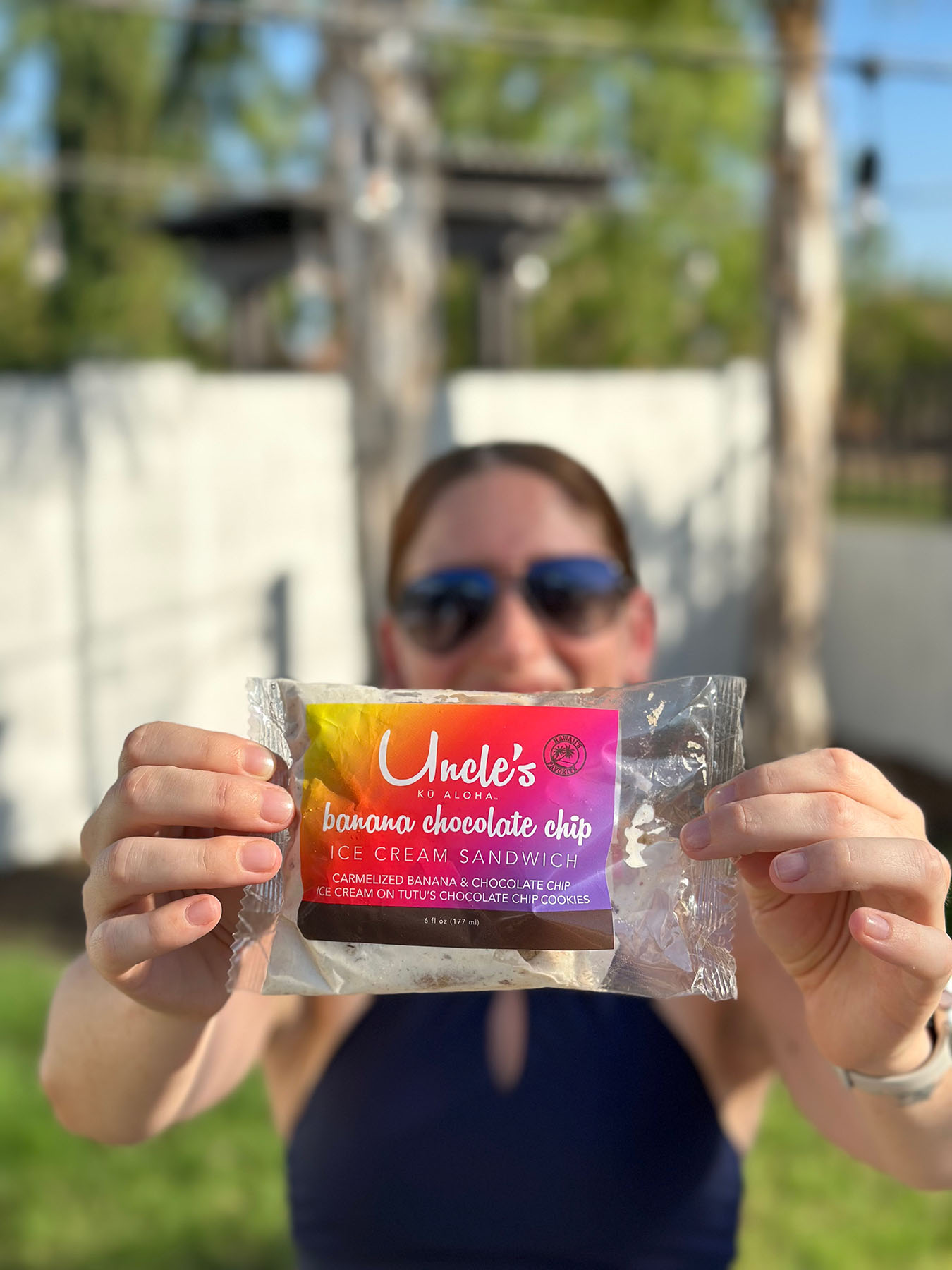 Julie Harris of Whiskey & Red holding up a client’s product, Uncle’s Banana Chocolate Chip Ice Cream Sandwich, outdoors. The packaging highlights the caramelized banana and chocolate chip flavor, symbolizing client collaboration and branding success.