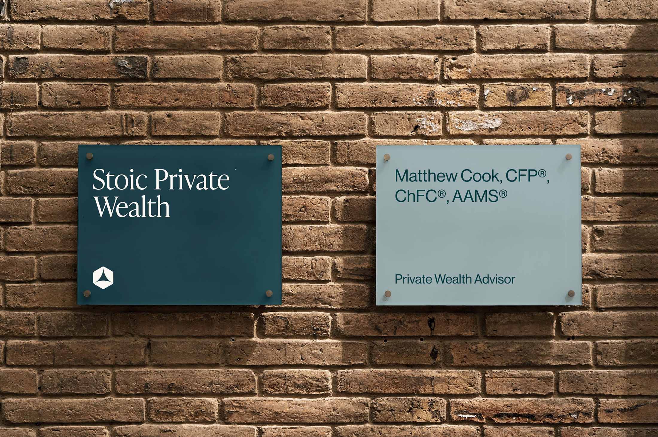 Stoic Private Wealth wall signage with the company logo and advisor credentials displayed on glass panels mounted on a brick wall.