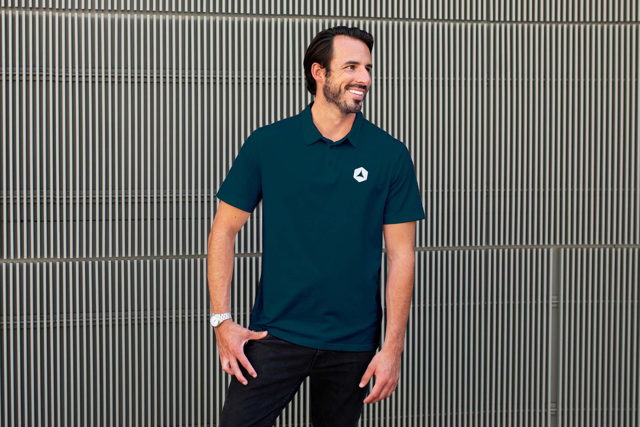 Man wearing a dark green polo shirt with the Stoic Private Wealth geometric logo, standing against a modern metal grid wall.