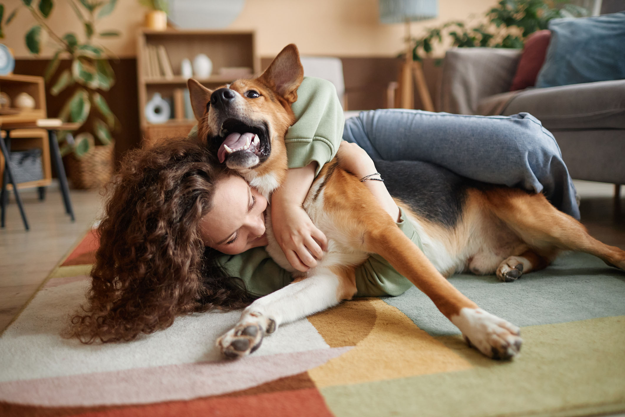 Smiling woman hugging her happy dog on a colorful area rug in a cozy living room, representing a pet-safe and family-friendly clean environment.
