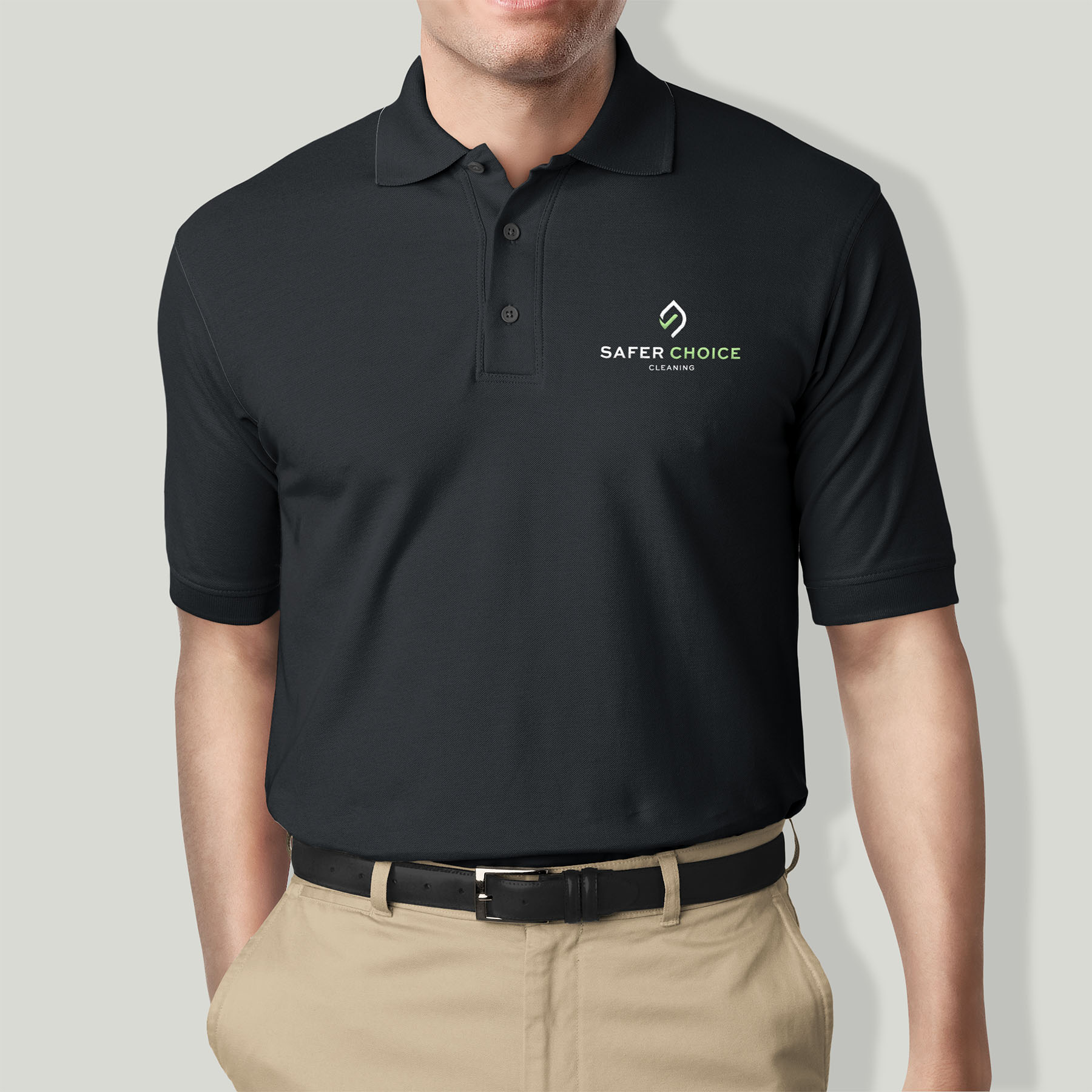Man wearing a black polo shirt embroidered with the Safer Choice Cleaning logo in green and white, paired with khaki pants, representing professional branded uniform design.