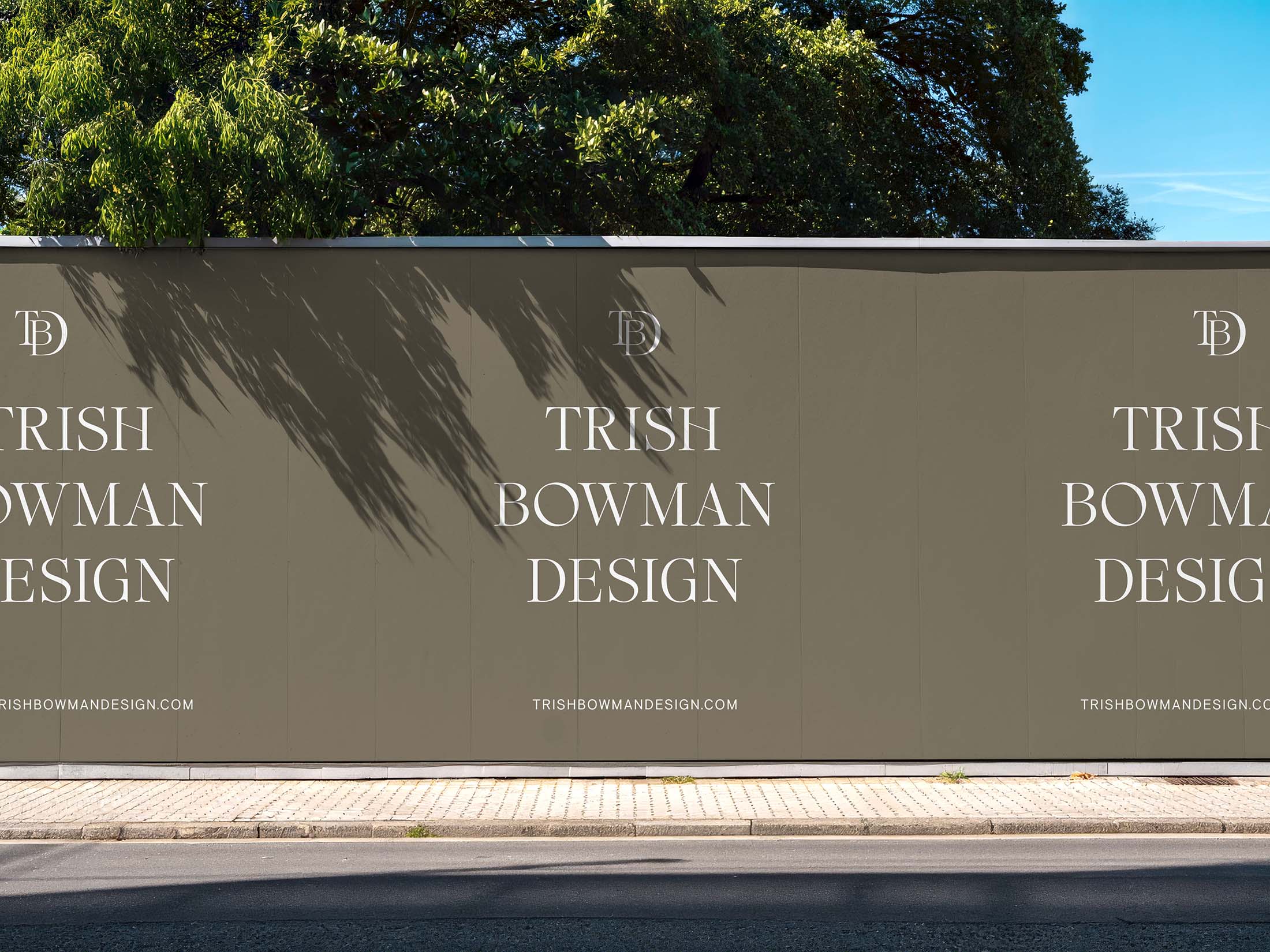 Alt text: Outdoor construction wall branded with the Trish Bowman Design logo and website, set against a backdrop of trees.