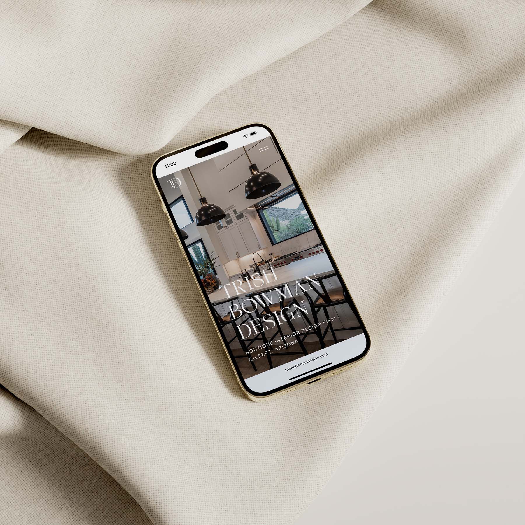 Alt text: Mobile view of the Trish Bowman Design website showcasing a modern kitchen, placed on soft beige fabric.