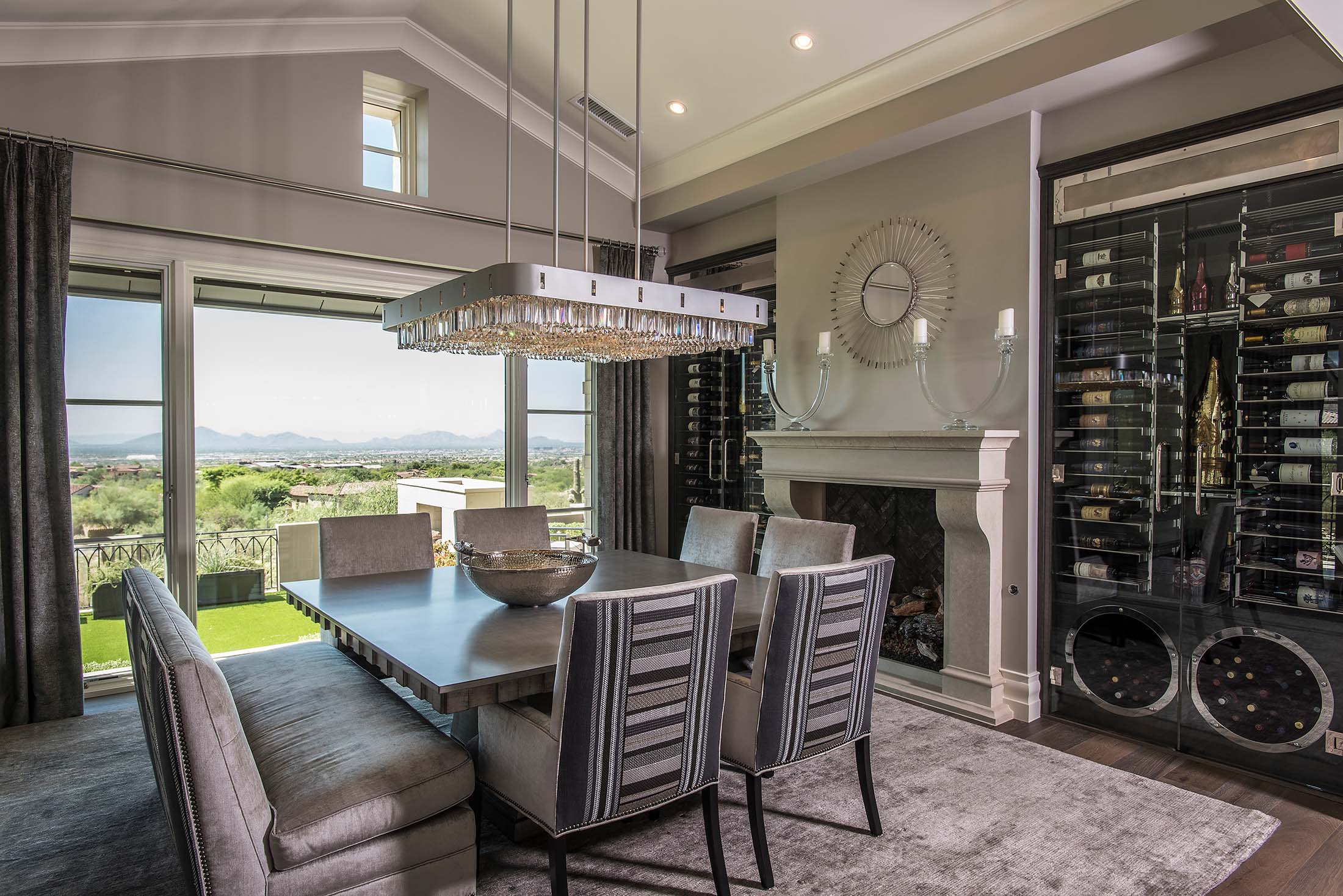 Formal dining room design featuring a crystal chandelier, fireplace, built-in wine storage, and panoramic mountain views.