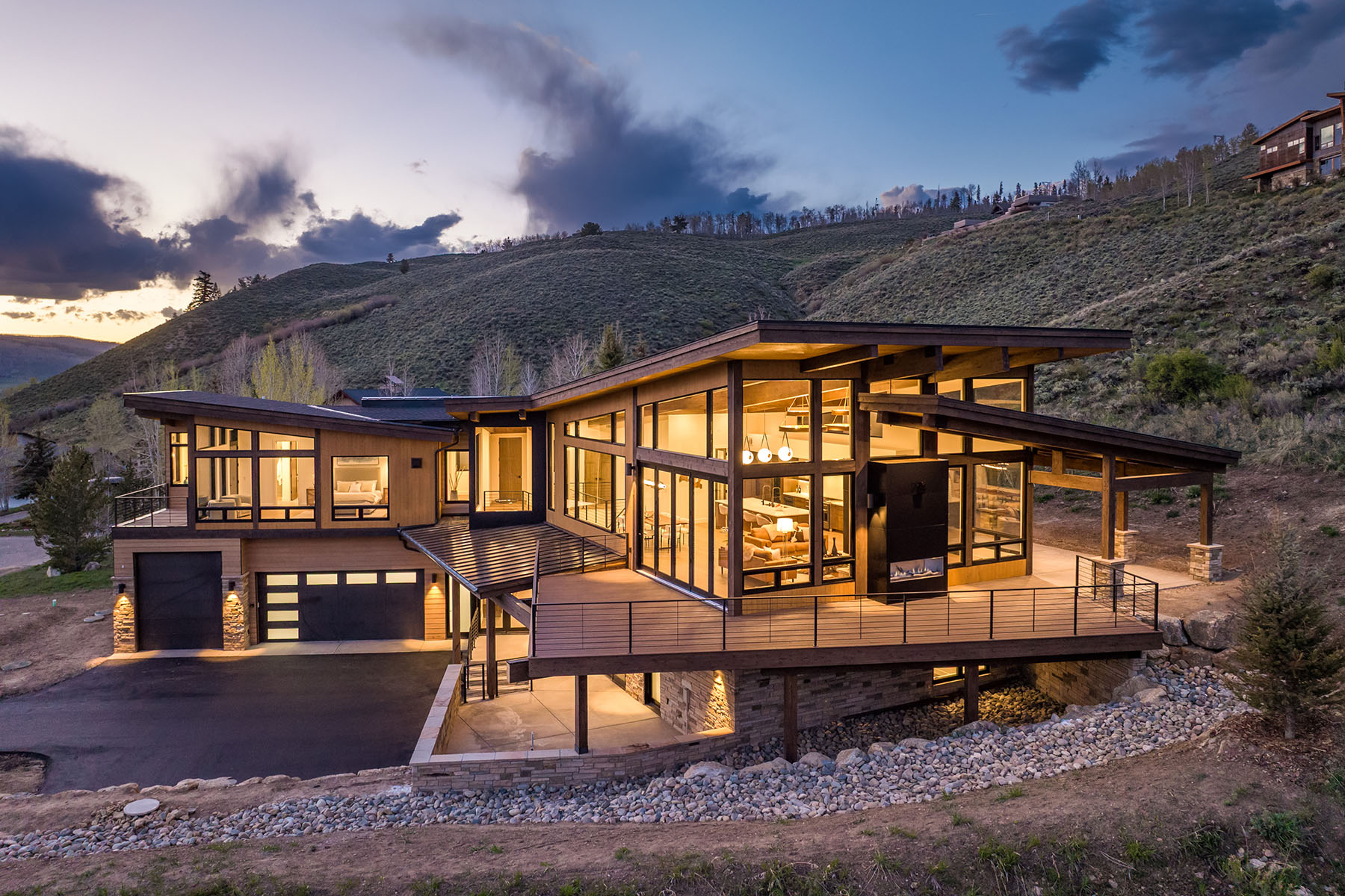 Modern custom mountain home in Summit County, Colorado with expansive windows, wood siding, and hillside views at dusk.